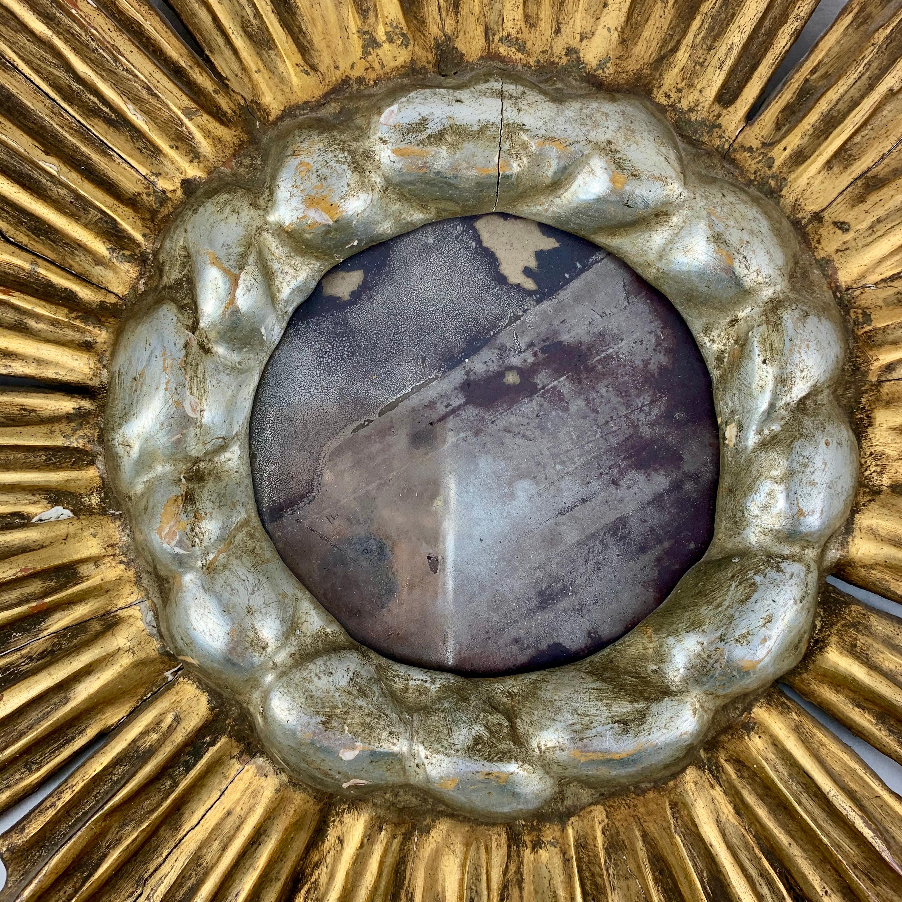 A Hollywood Regency Period wall mirror, showing a giltwood sunburst with a cloud bezel, from France, circa 1920s.

Made of gilded and silvered gesso on wood, the mirror is set in a bezel resembling clouds painted in a soft silvery gold. The gilded