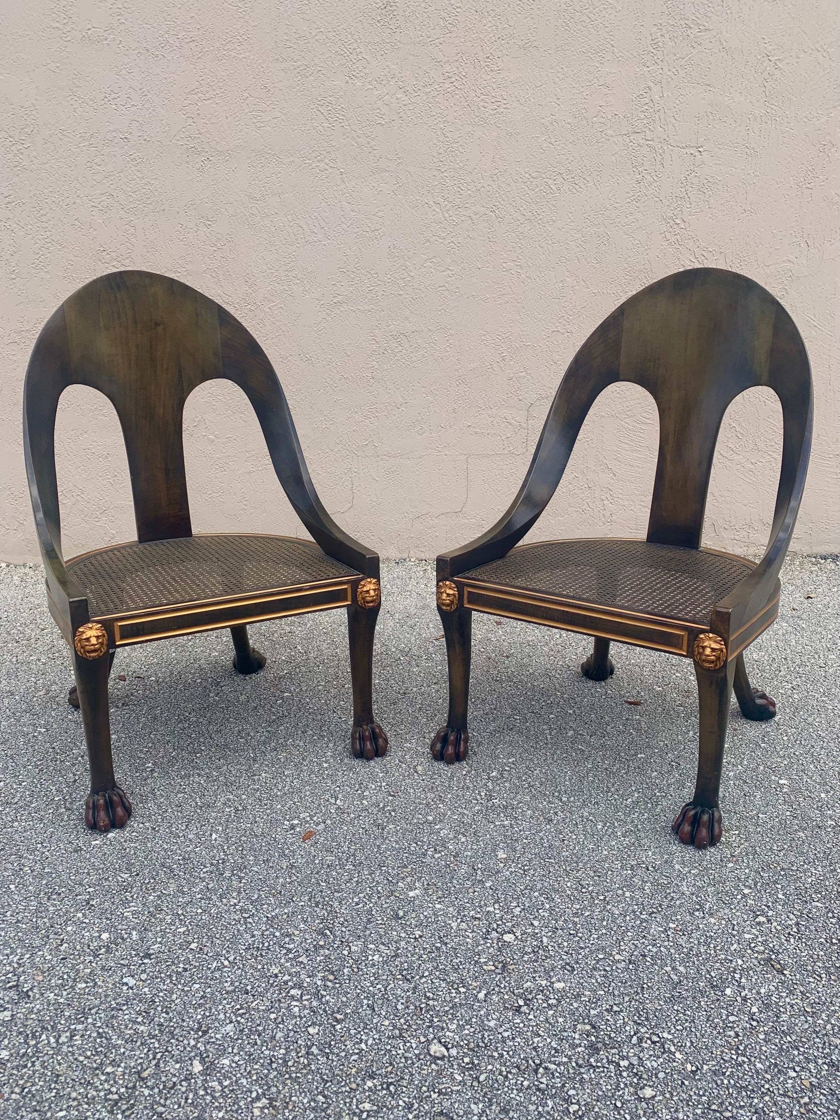 Pair of elegant spoonback chairs by Baker Furniture. Hollywood regency style shapes and accents with beautiful details of claw feet, lions heads, and inlay channels. The channels and lions head are gilt finished and there is an undertone of red