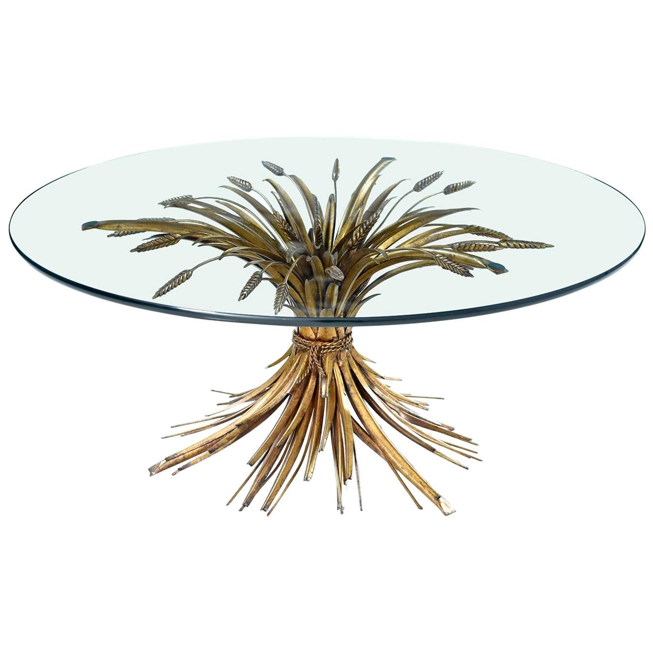 Elegant and luxurious, this Italian Hollywood Regency table glamorizes the humble wheat sheaf. The coffee table is made of sculpted metal with a gold gilt finish and topped with a piece of circular glass. The circle glass top balances on top of the