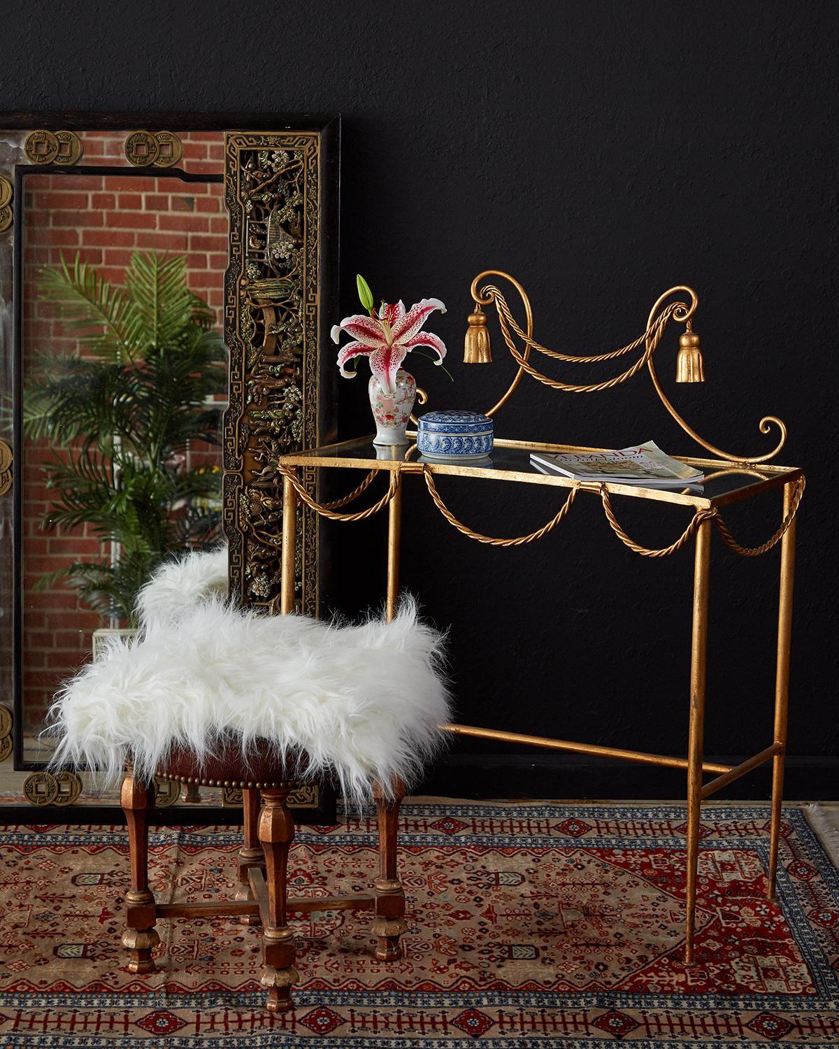 Diminutive gilt iron and faux rope vanity or console table made in the glamorous Hollywood Regency taste. Features a gilded iron frame decorated with iron rope swag and tassels. The top is scalloped with a glass insert and is supported by elegant