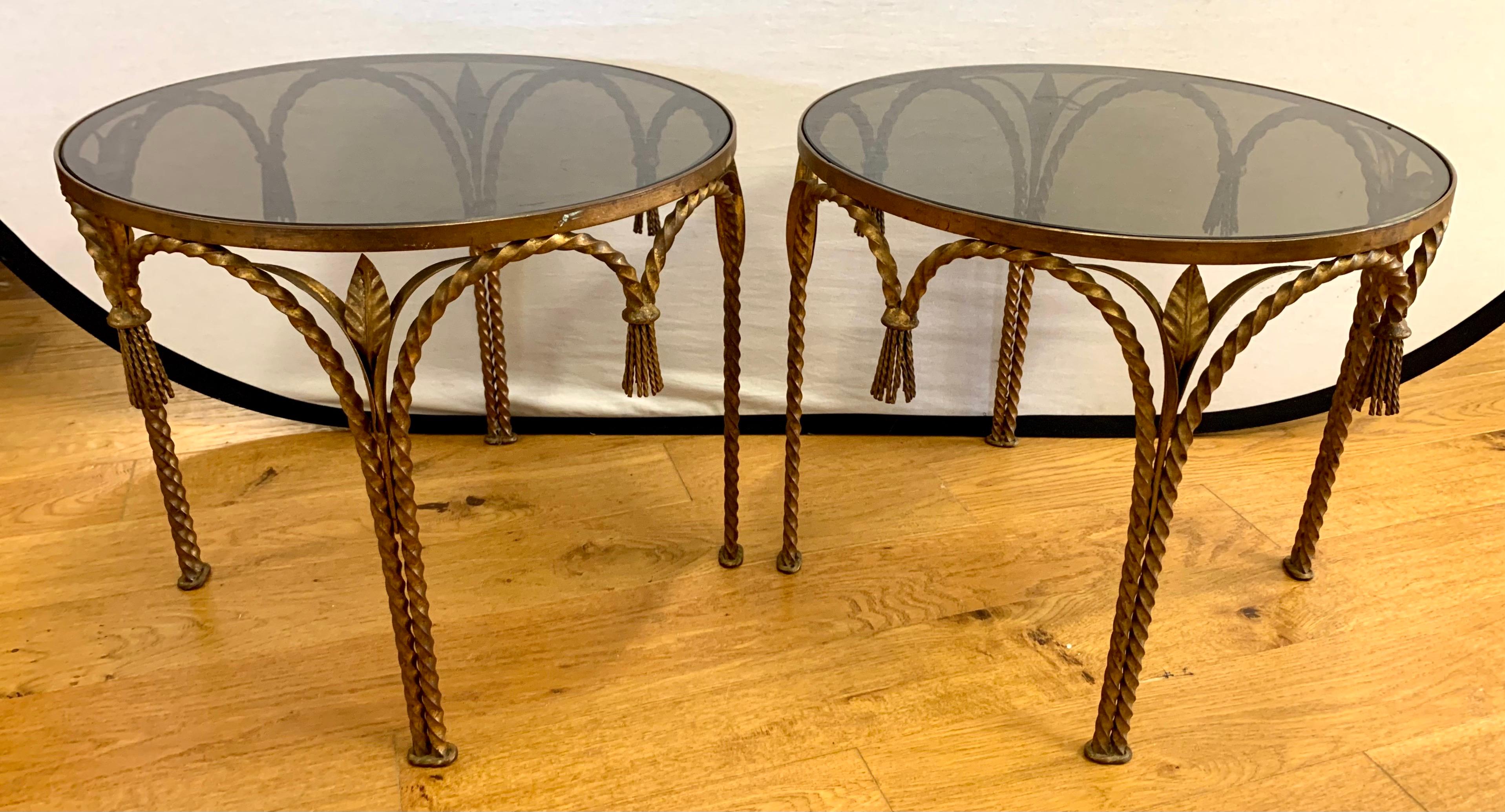 A pair of matching Hollywood Regency gilt metal rope and tassel round end tables with smoked glass tops.