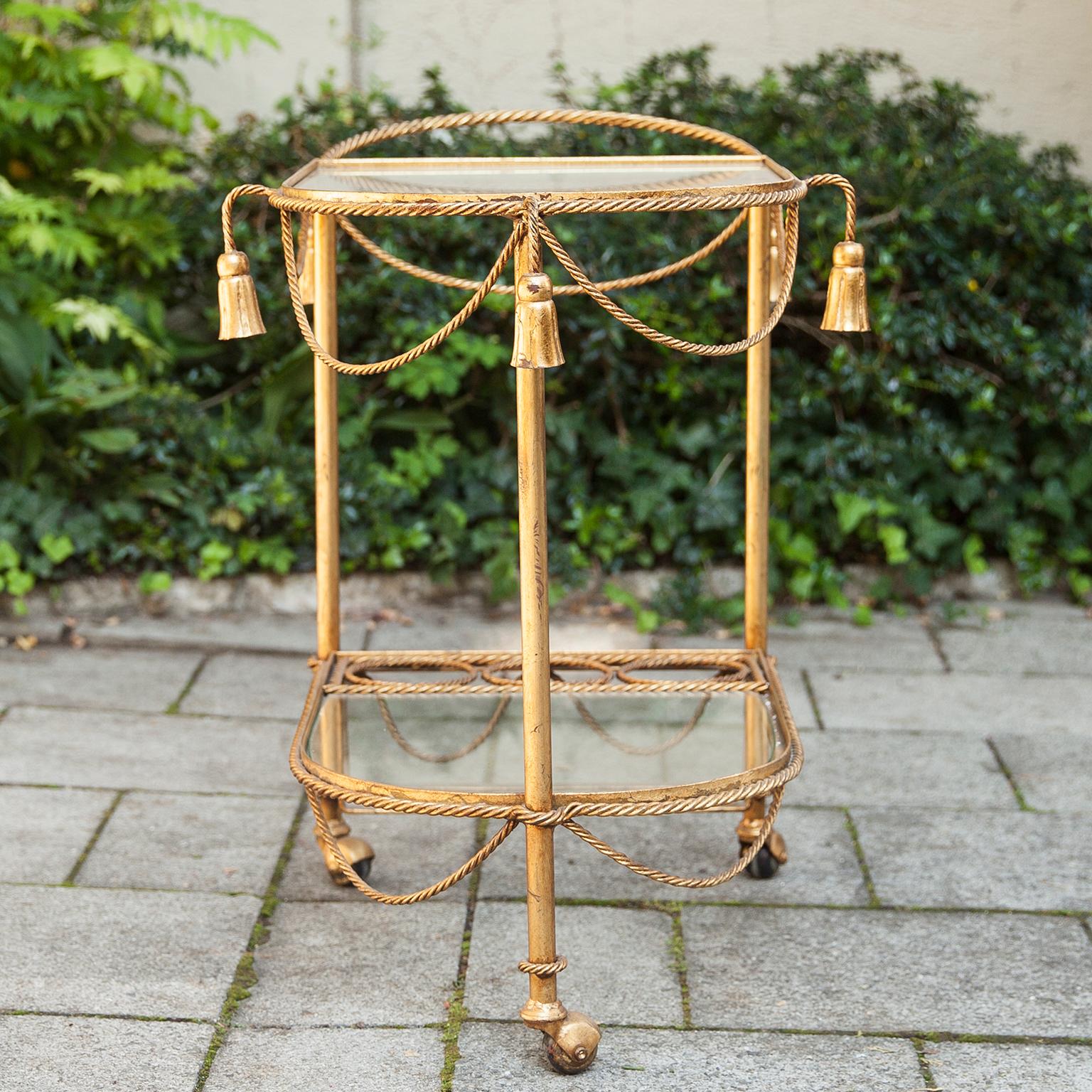 A beautiful Hollywood Regency gilt metal rope and tassel bar cart with glass tops, Italy Florence, 1970s.

 