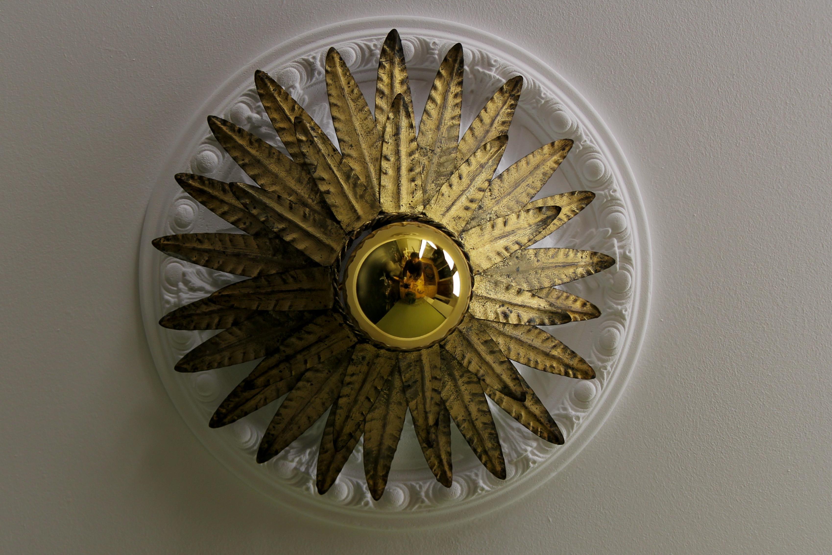 Hollywood Regency gilt metal sunburst-shaped crown ceiling light fixture, Spain, circa the 1960s.
This outstanding sunburst-shaped or crown-shaped ceiling light features two layers of gilt metal leaves surrounding the central exposed bulb.
This