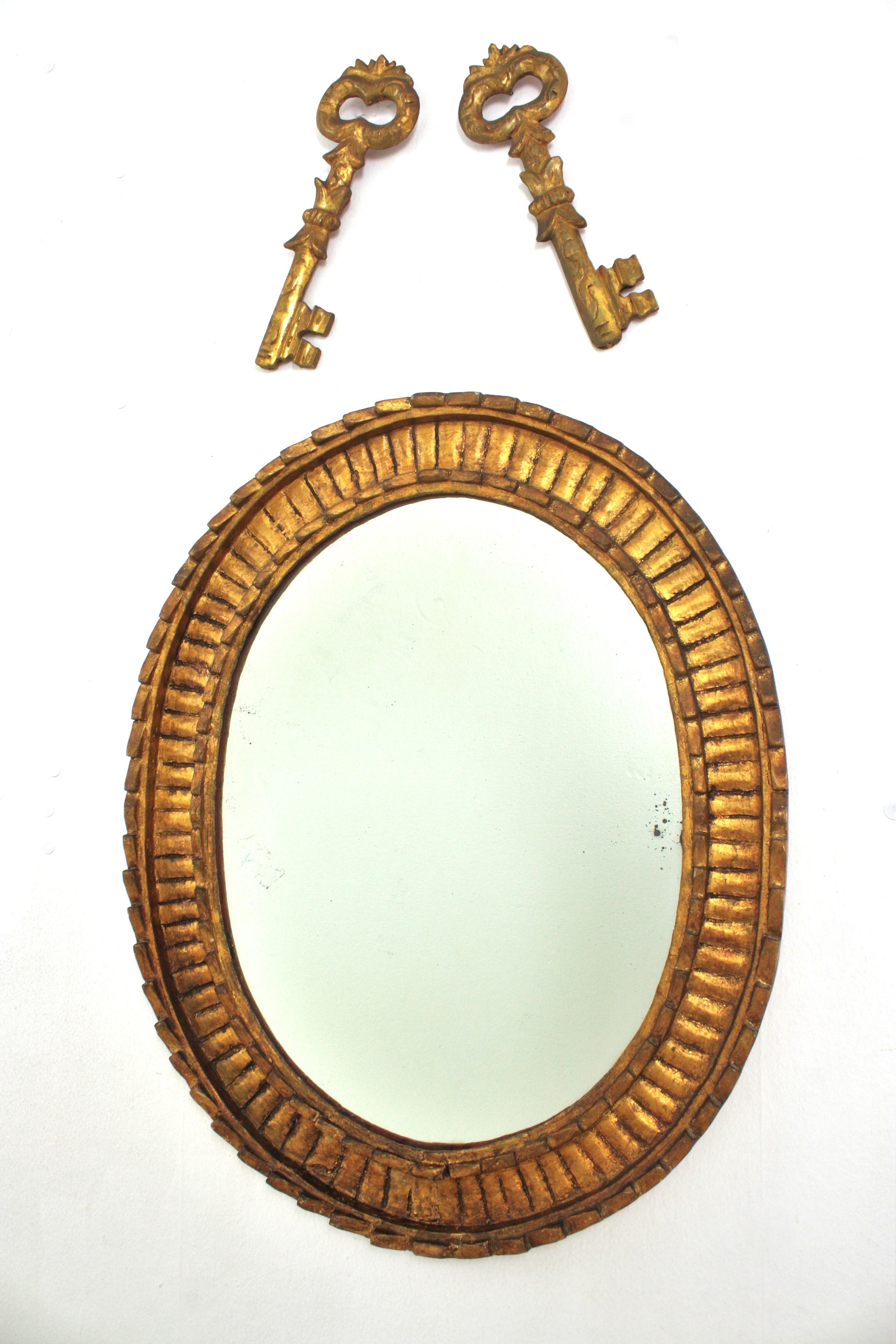 Magnifique miroir mural ovale en bois doré festonné avec décoration de clés sculptées, finition à la feuille d'or, style Hollywood Regency. Espagne, années 1950
Fabriqué par l'ébéniste espagnol Francisco Hurtado. 
Une trouvaille rare.
Ce miroir