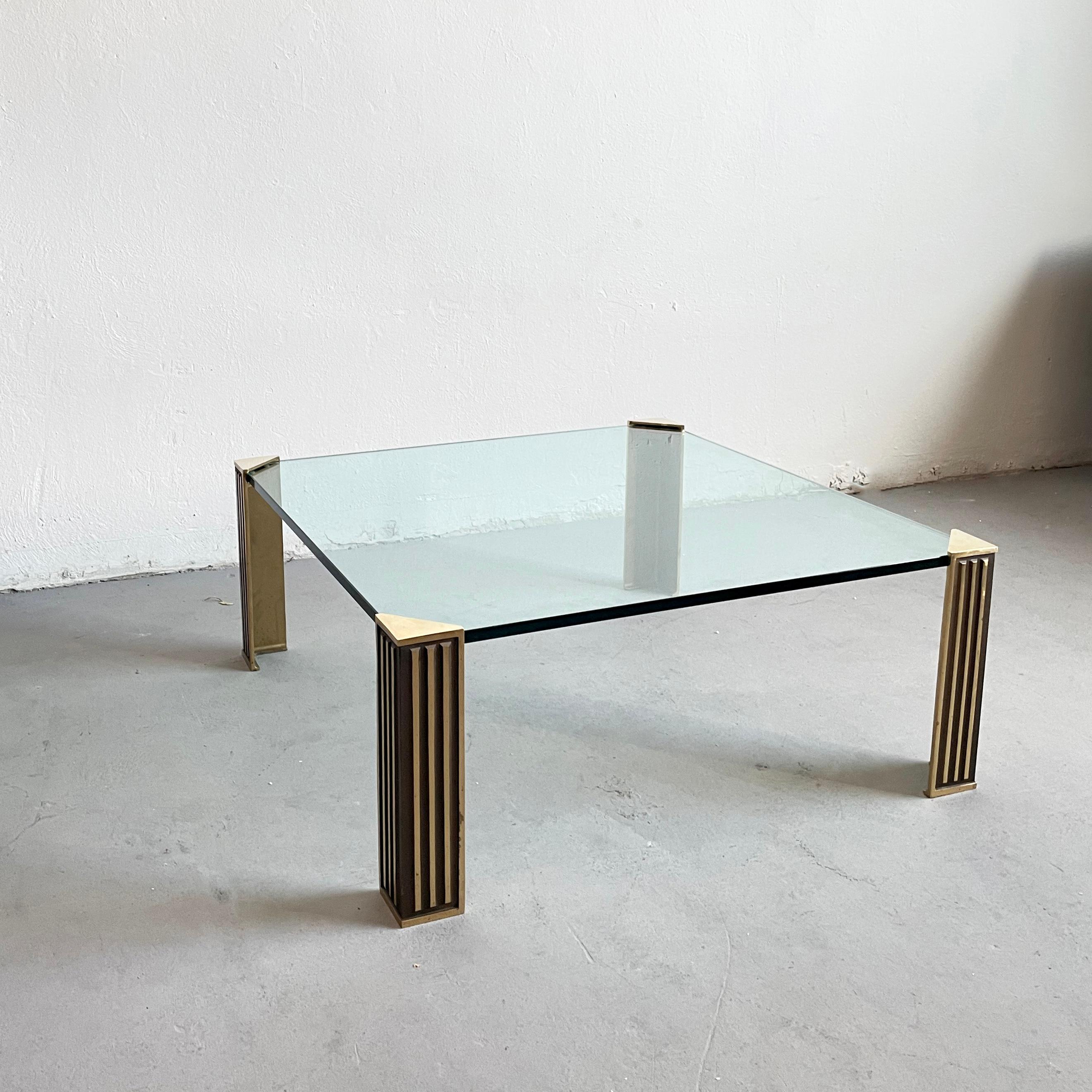 Élégante table basse Hollywood Regency composée d'un plateau en verre teinté et de pieds en laiton

Le verre mesure 100 x 100 x 1,5 cm et il est très lourd.

L'état de la table est très bon, présentant juste de petites traces d'usure