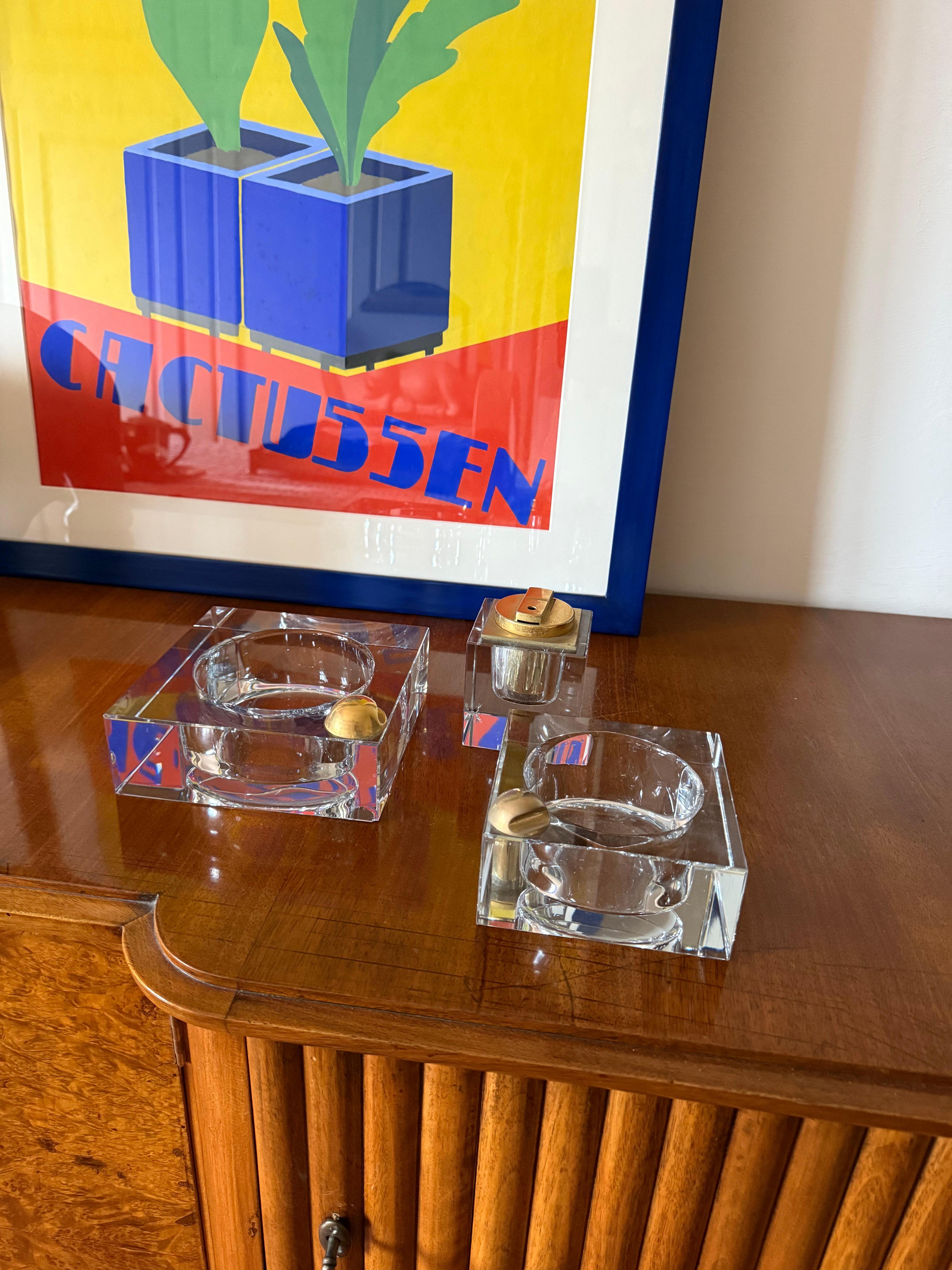 Ensemble de fumeurs en verre Hollywood Regency. 2 cendriers, 1 briquet de table

France années 1970

Verre, laiton

H 5,5 cm - 12 × 12 cm

H 5,5 cm - 15 × 15 cm

H 9 cm - 7 × 8 cm

Etat : très bon, conforme à l'âge et à l'usage, Petit éclat sur le
