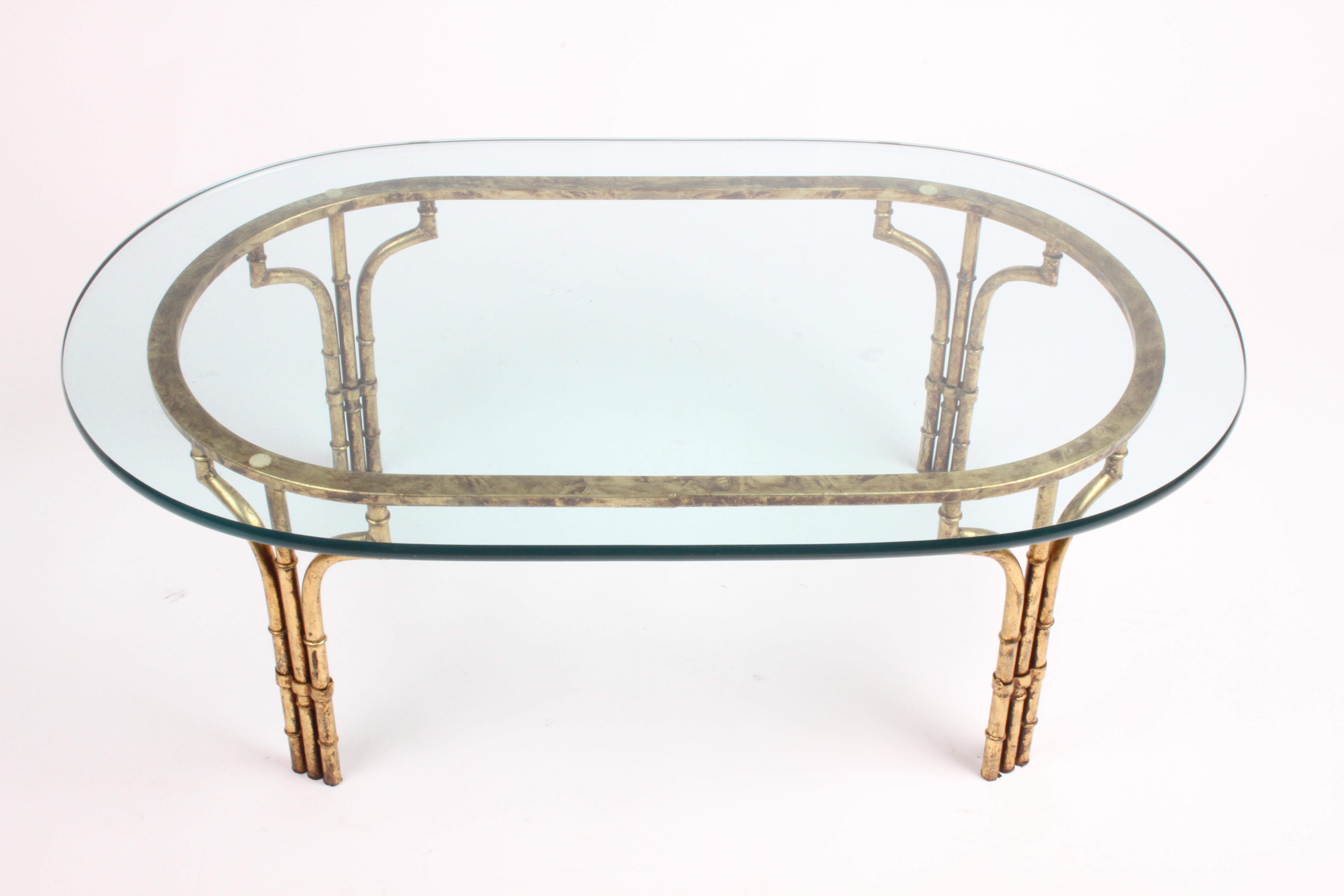 Table basse italienne Vintage Hollywood Regency en faux bambou doré avec plateau en verre ovale 3/4 d'épaisseur. La base en fer en forme de faux bambou a une finition dorée antique, qui est en bon état, avec des pertes mineures, mais qui a encore de