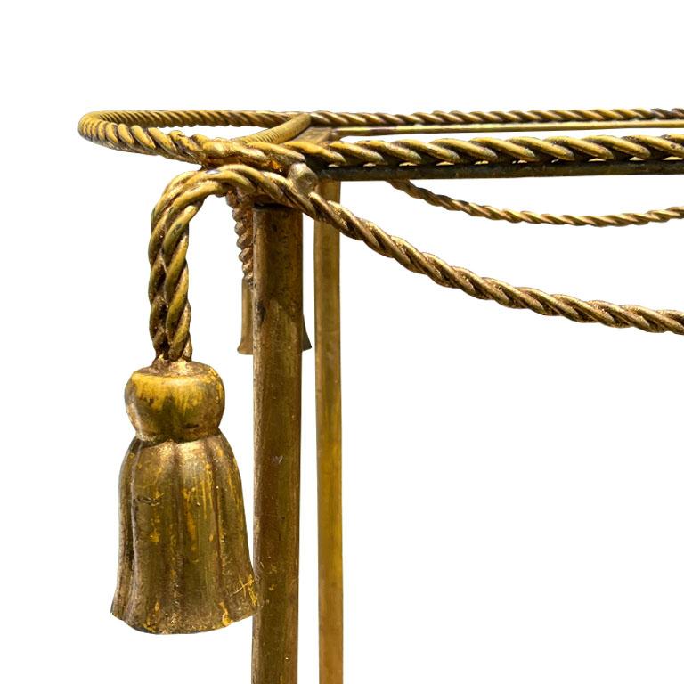 A vintage gold Italian faux tassel and rope metal rolling bar cart. This beautiful Hollywood Regency beverage cart will be the star of the show at your next cocktail party. It is rectangular in form, with a curved end on one side, and a braided