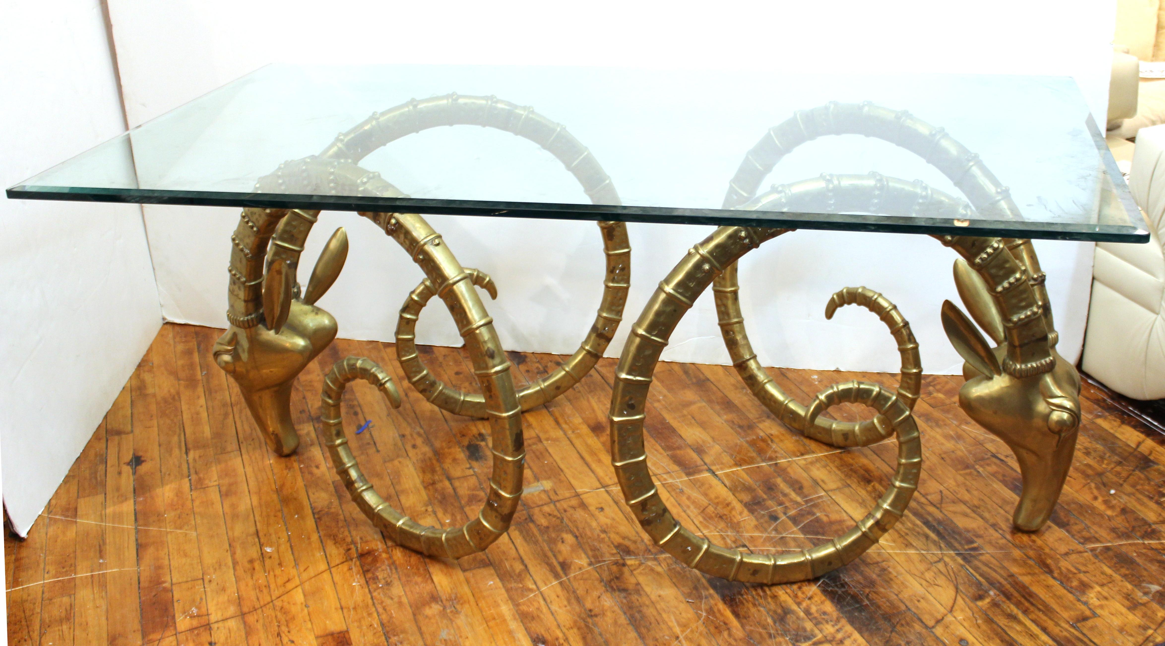 Hollywood Regency brass ibex head dining table with thick glass top, attributed to Alain Chervet. The heads have age-appropriate patina and some tarnish in a few spots, but overall in great vintage condition.