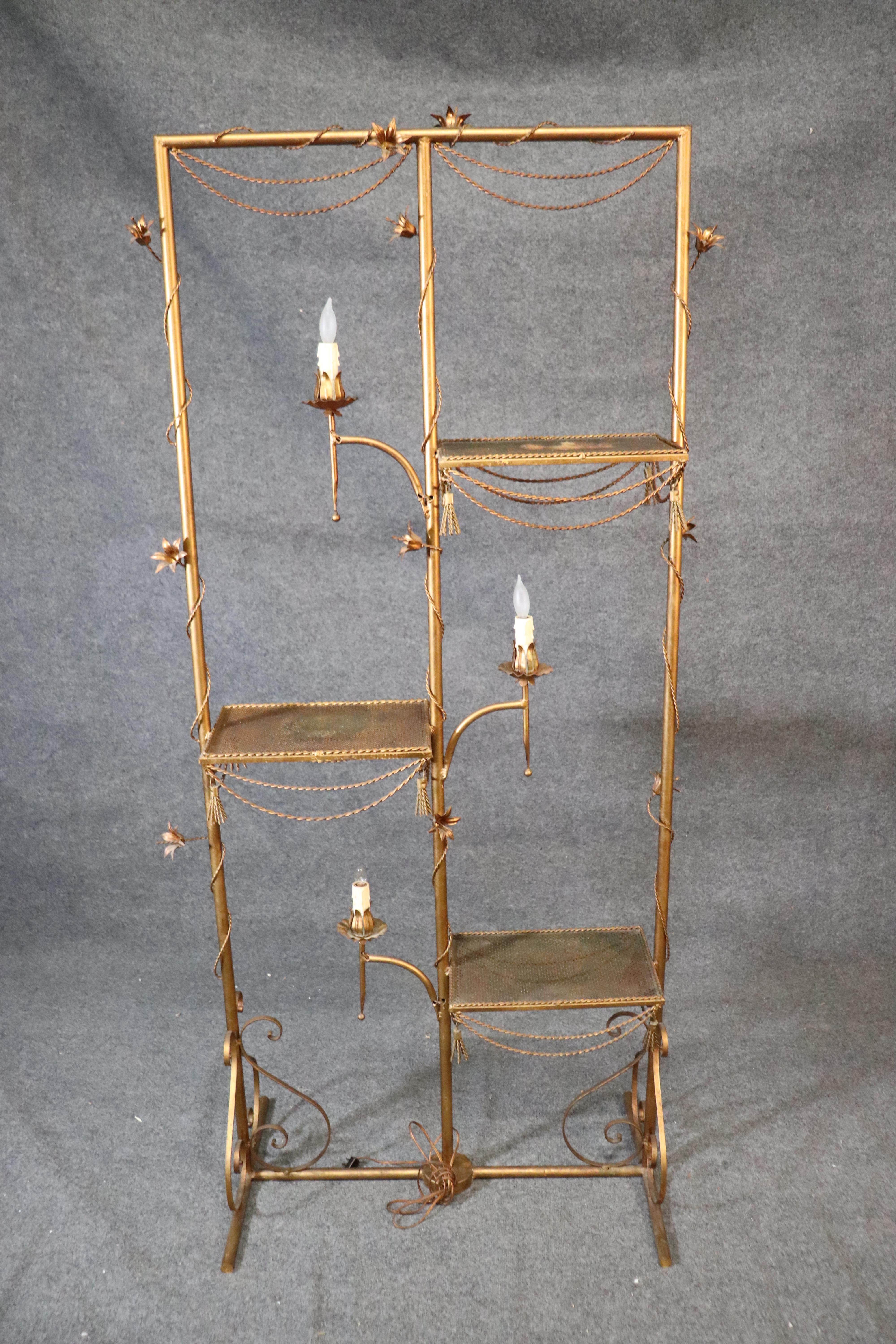 This is a rare item indeed. This is a great Italian made gilded metal tole étagère done in the Hollywood Regency tradition dating to 1950. The étagère features candle-form lights and flowers and tassels. The étagère measures 75 tall x 36 wide x 10