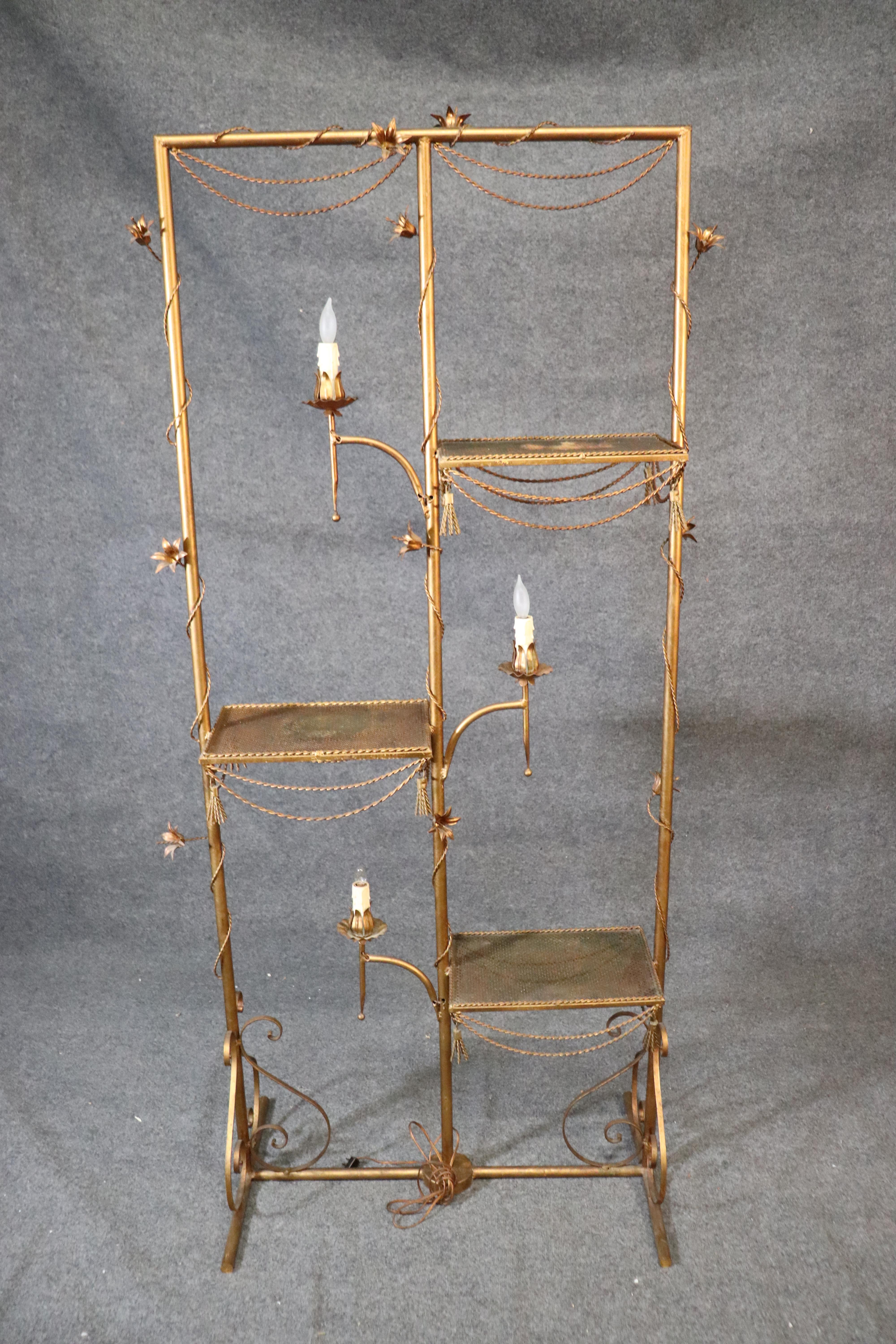 This is a rare item indeed. This is a great Italian made gilded metal tole étagère done in the Hollywood Regency tradition dating to 1950. The étagère features candle-form lights and flowers and tassels. The étagère measures 75 tall x 36 wide x 10