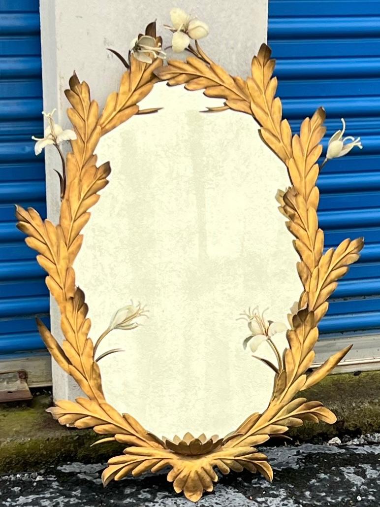 This is a sweet Italian tole mirror! Its oval frame is comprised if what appears to be laurel leaves and ivory flowers. The gilt metal is in very good condiment. It dates to the 1960s and is unmarked.