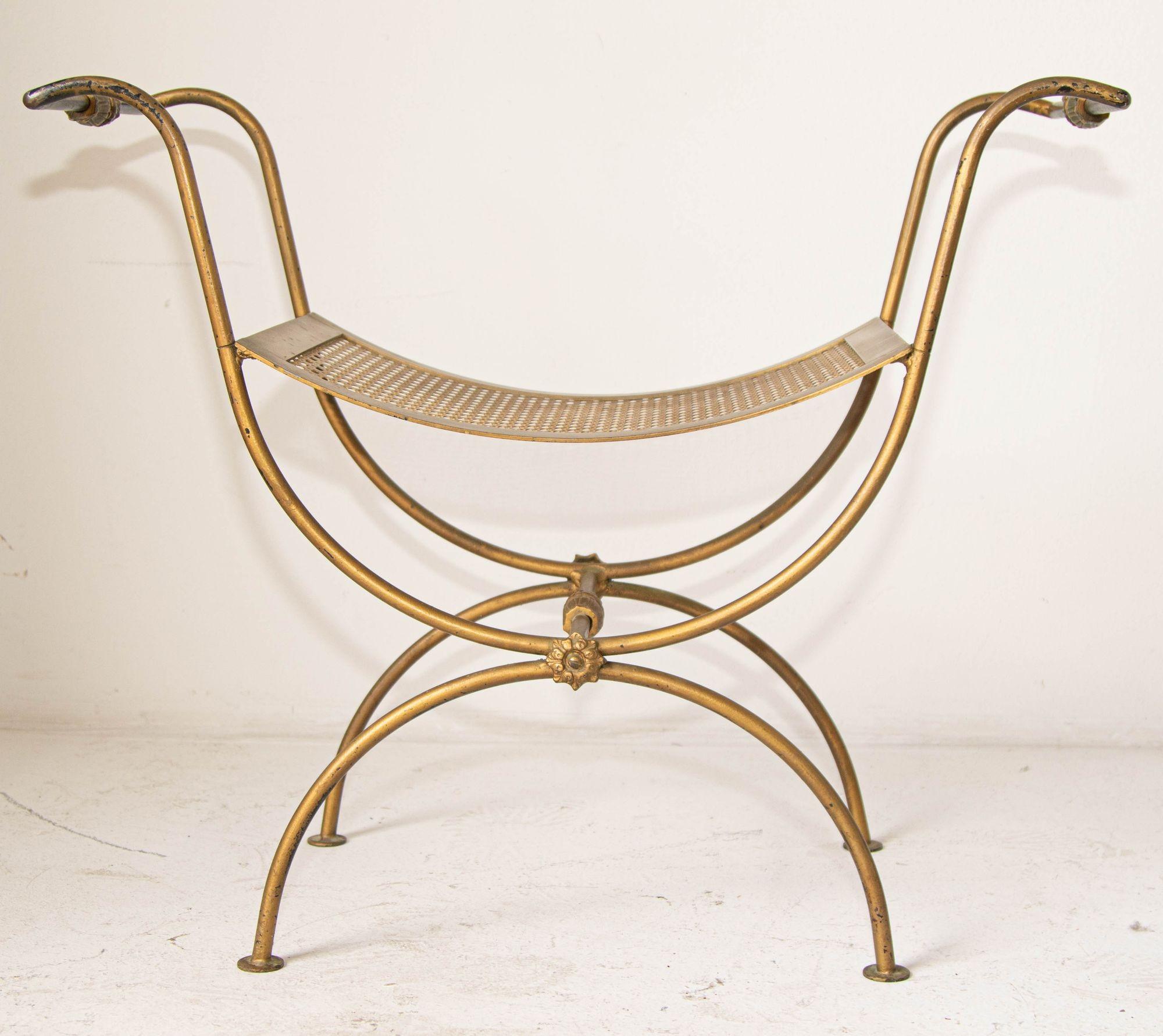 Vintage midcentury Hollywood Regency, Italian gilt metal bench with rich patina.
Midcentury gilt metal curule form bench with a curved base and curved seat, accented with brass rosettes.
The curule bench is a design well-noted for its use by Roman
