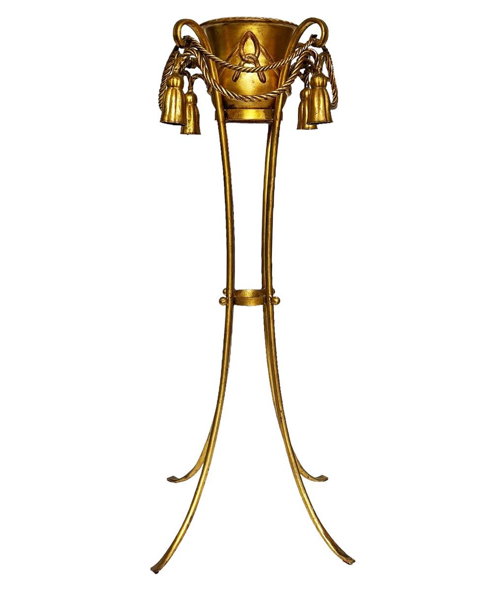 Una fioriera alta con motivo di corde e nappe in oro dorato. Un pezzo versatile e decorativo da utilizzare in qualsiasi stanza della casa. Acciaio dorato e legno. 