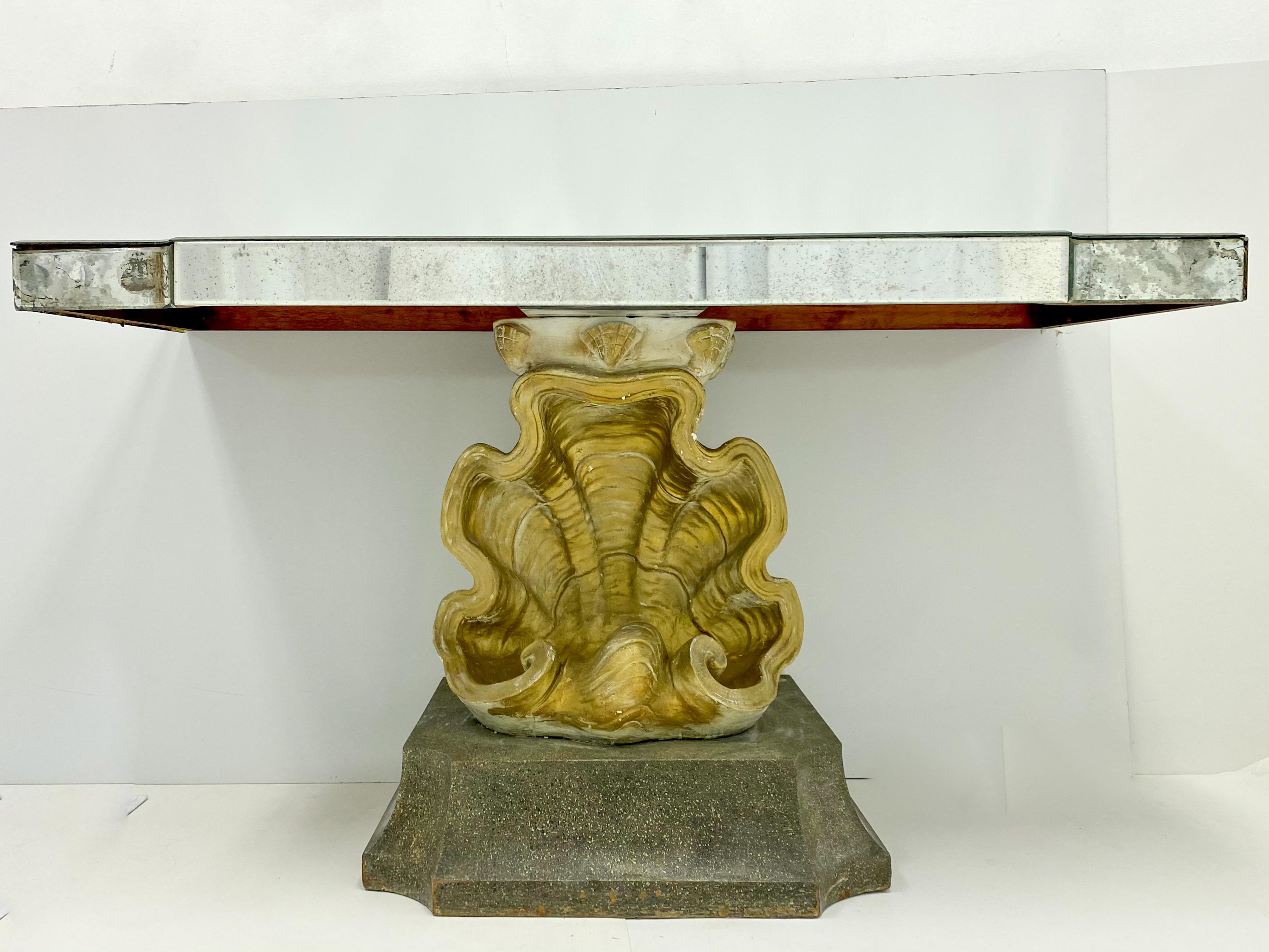 This is a Hollywood Regency Era mirrored console table. The top is intentionally distressed mirror. The gilt shell is plaster. The back of the shell is painted to look more like a natural clam. The base is painted wood and measures: 28” L. Height to