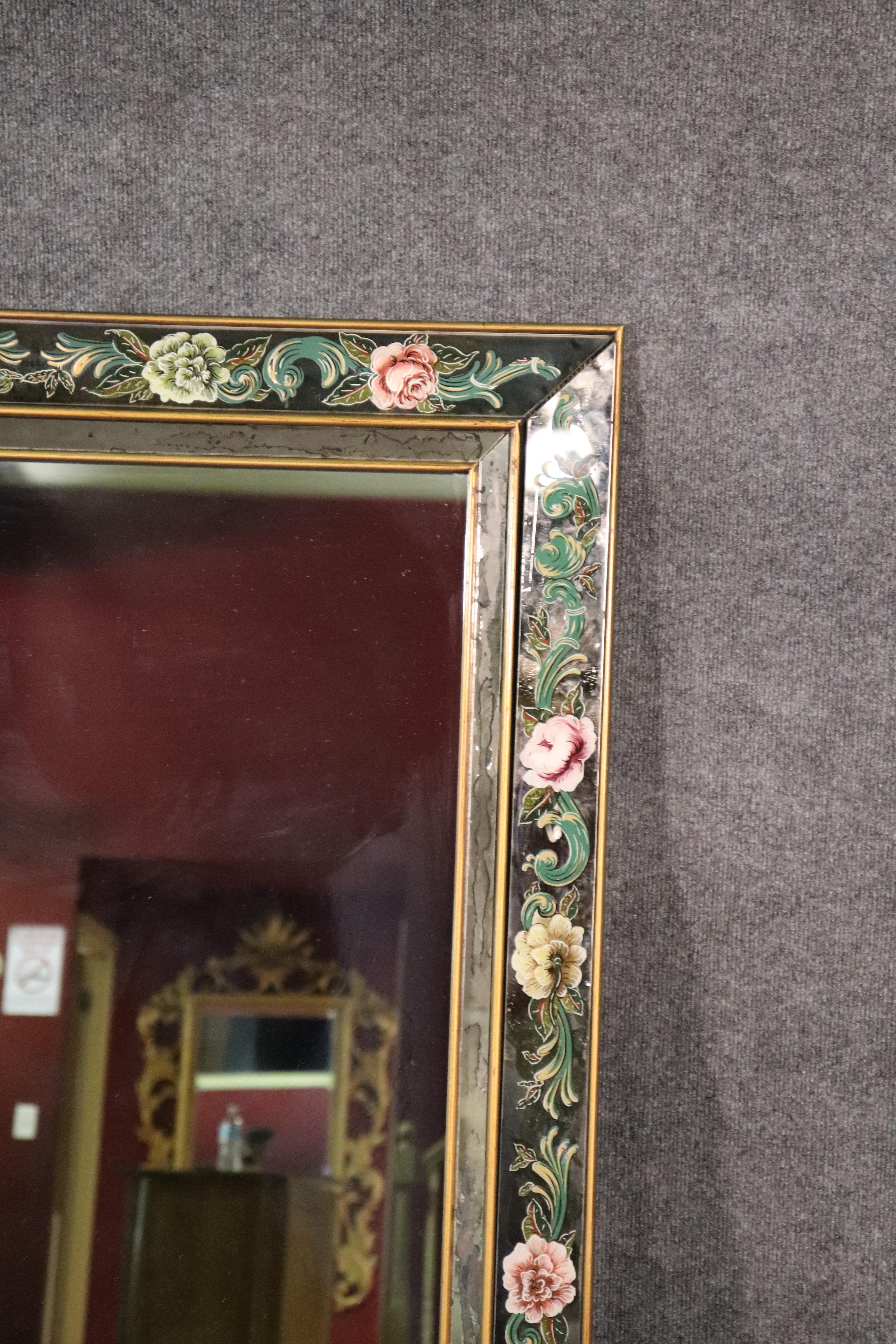 This is a great mirror that dates to the 1950s era and has a cushion style to it, as the edges of the mirror are dimensional and not flat. The glass as well as the paint decorated églomisé flowers are in good condition. The mirror is perfect for