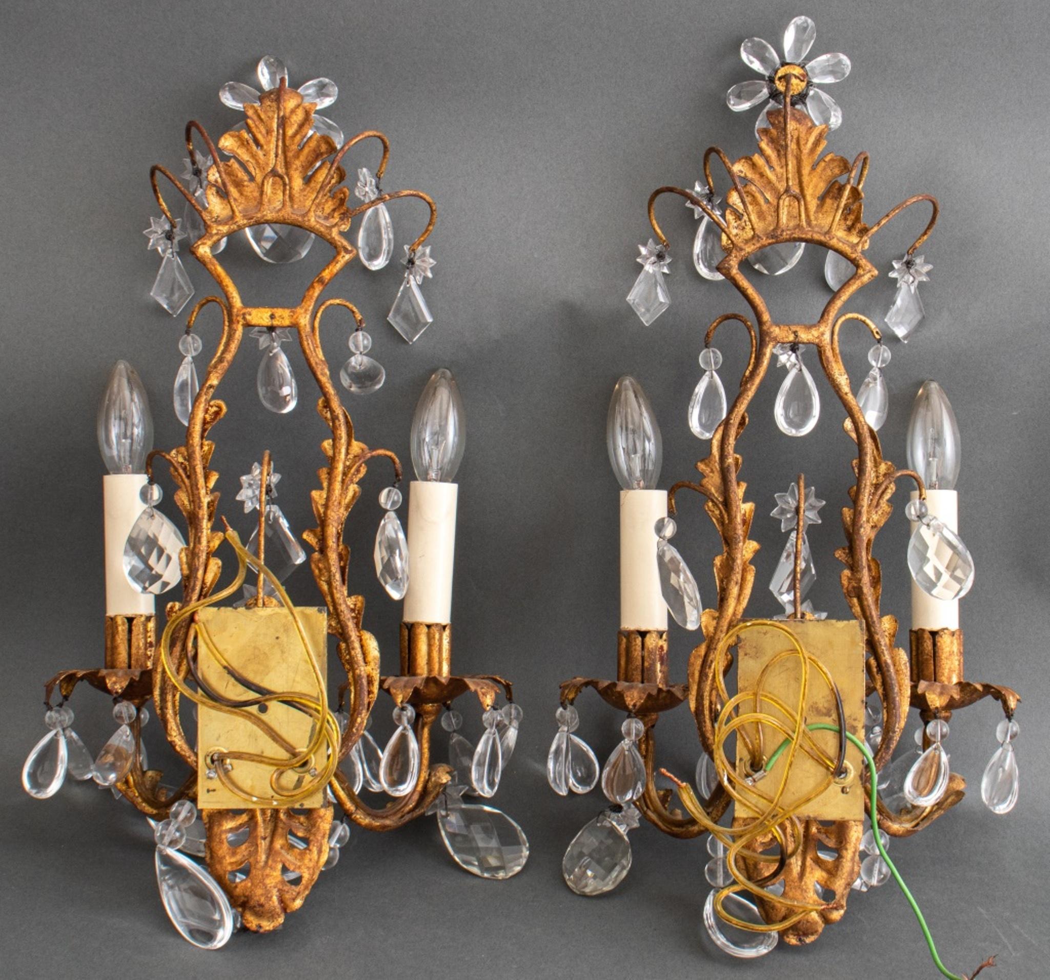 Hollywood Regency Italian Rococo Revival two-light sconces, 1960s-1970s, each with reticulated scrolling gilt metal mounts on a gilt metal cage frame issuing three arms, the whole hung with crystals and wired with floriform ornaments. In very good
