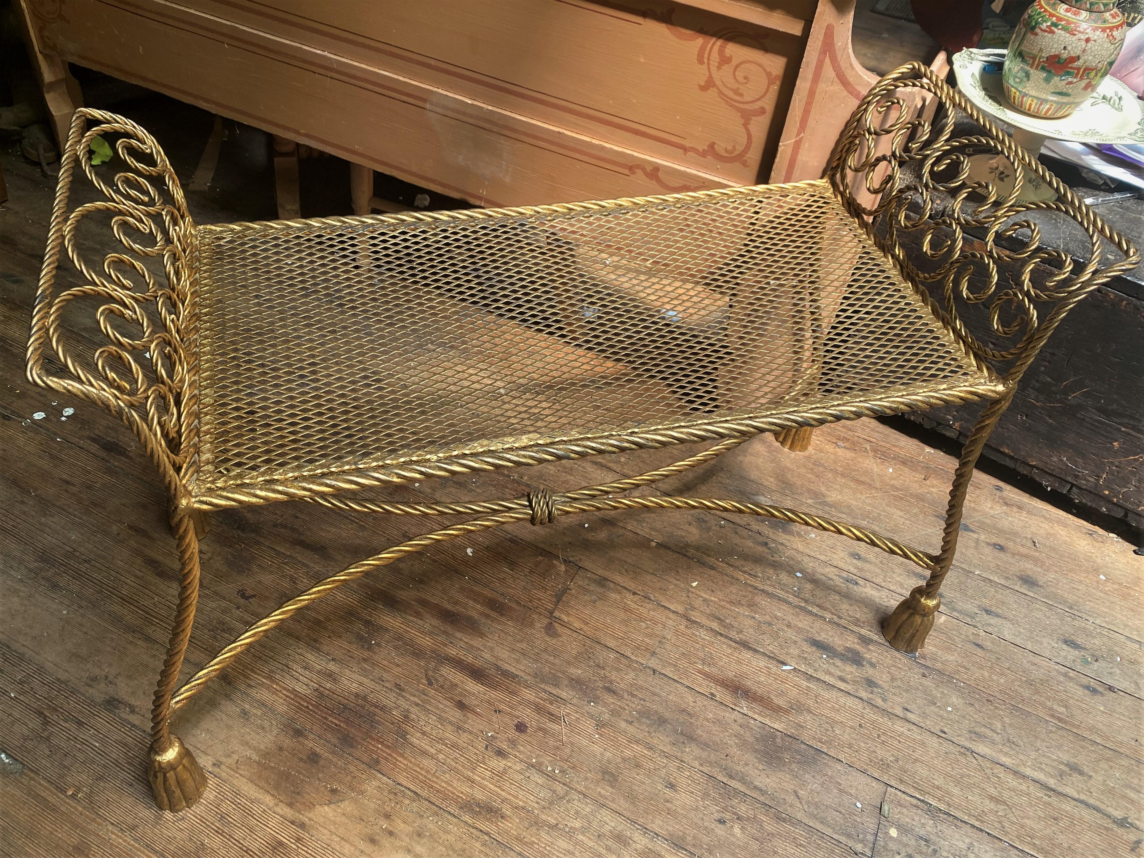 This is a very nice gold finished metal bench with rope twist around the outside, legs and swirled into an arched pattern on each end. The feet are fun gold faux tassels and the stretcher is also twisted rope design bound in the center. The seat is