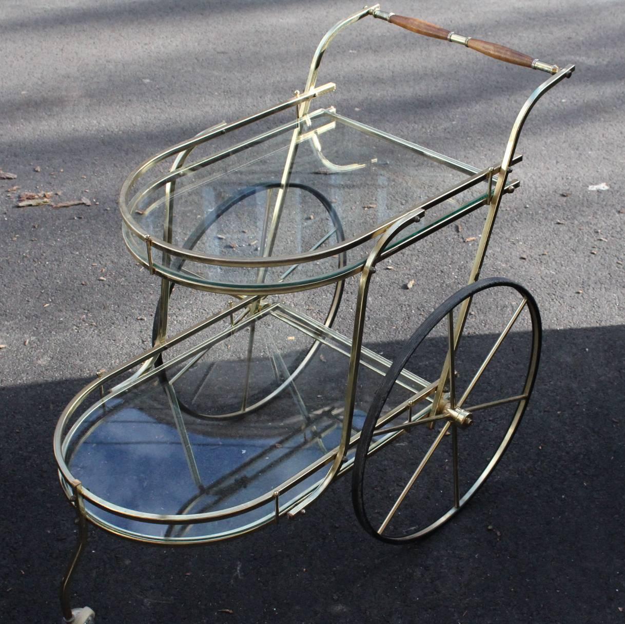 Hollywood Regency Italian two-tier bar cart or tea trolley in polished brass and glass dating from circa 1950. The cart features glass tiers with galleries, two large spoke wheels and a front caster wheel. The cart is in good vintage condition and