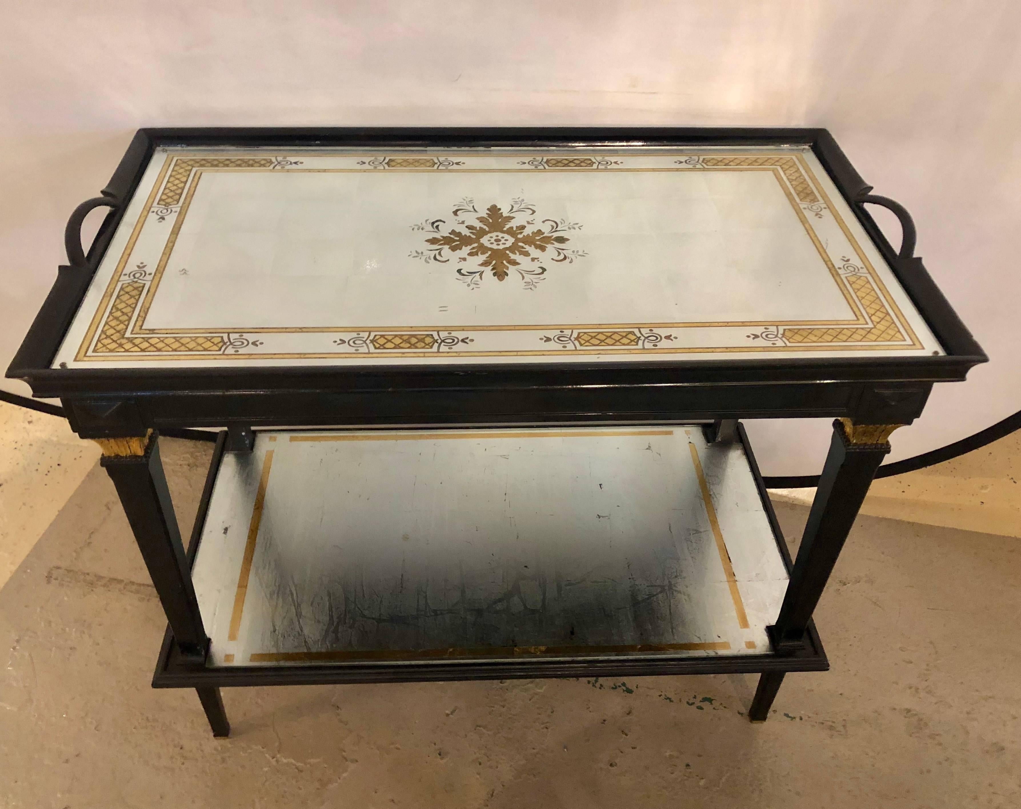 A fine Jansen two-tier serving cart having an églomisé removable tray top on an ebonized frame. This wonderfully decorative Hollywood Regency table has a mirrored design upper lift off serving tray top on an ebony base with a lower mirrored and