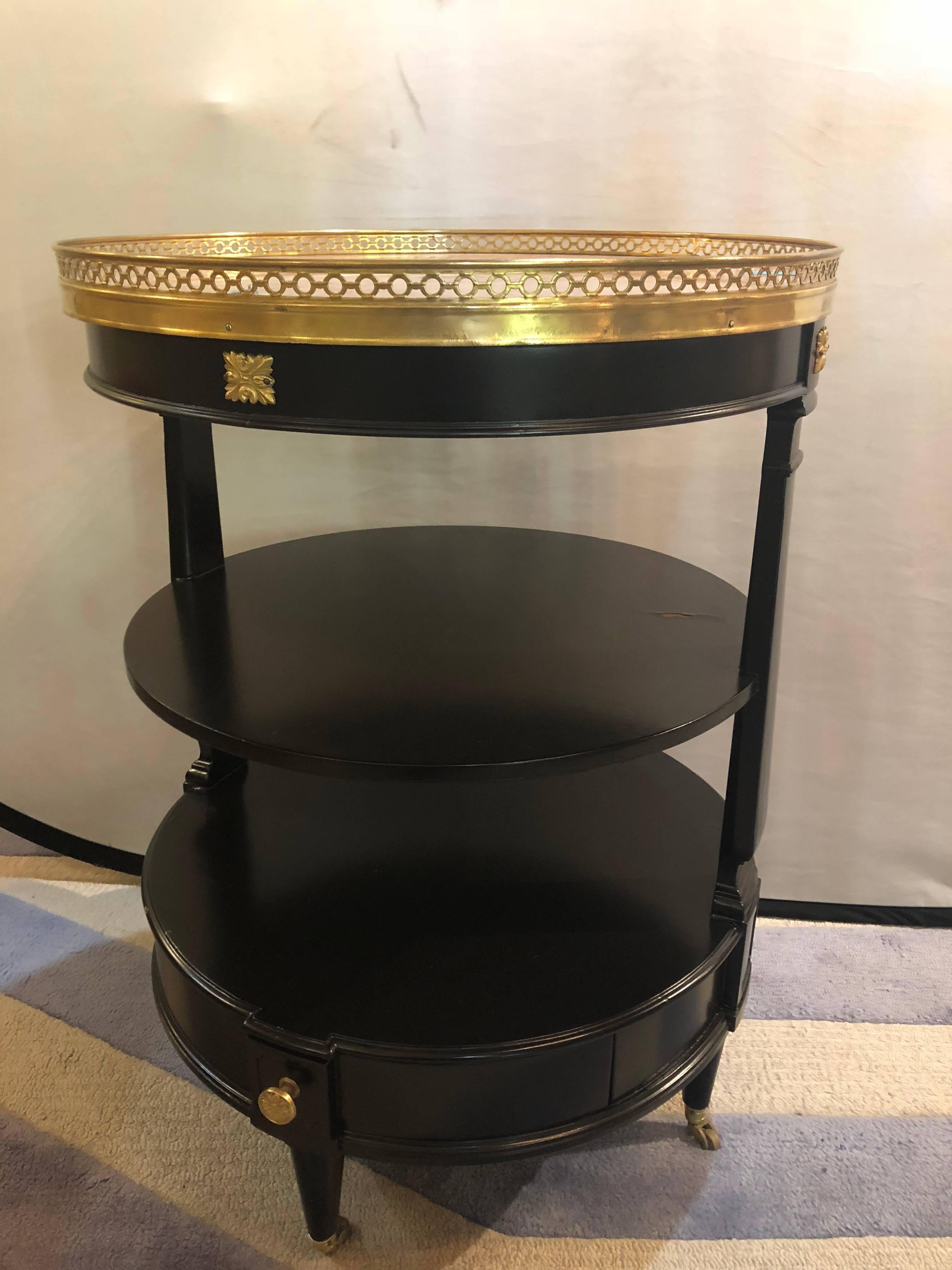 A three-tier Jansen style ebonized dumbwaiter bronze mounted with a marble top. A single oak secondary drawer on the bottom leading to three shelves, the top with a bronze pierced galleried marble. Having bronze decorative mounts on the apron as