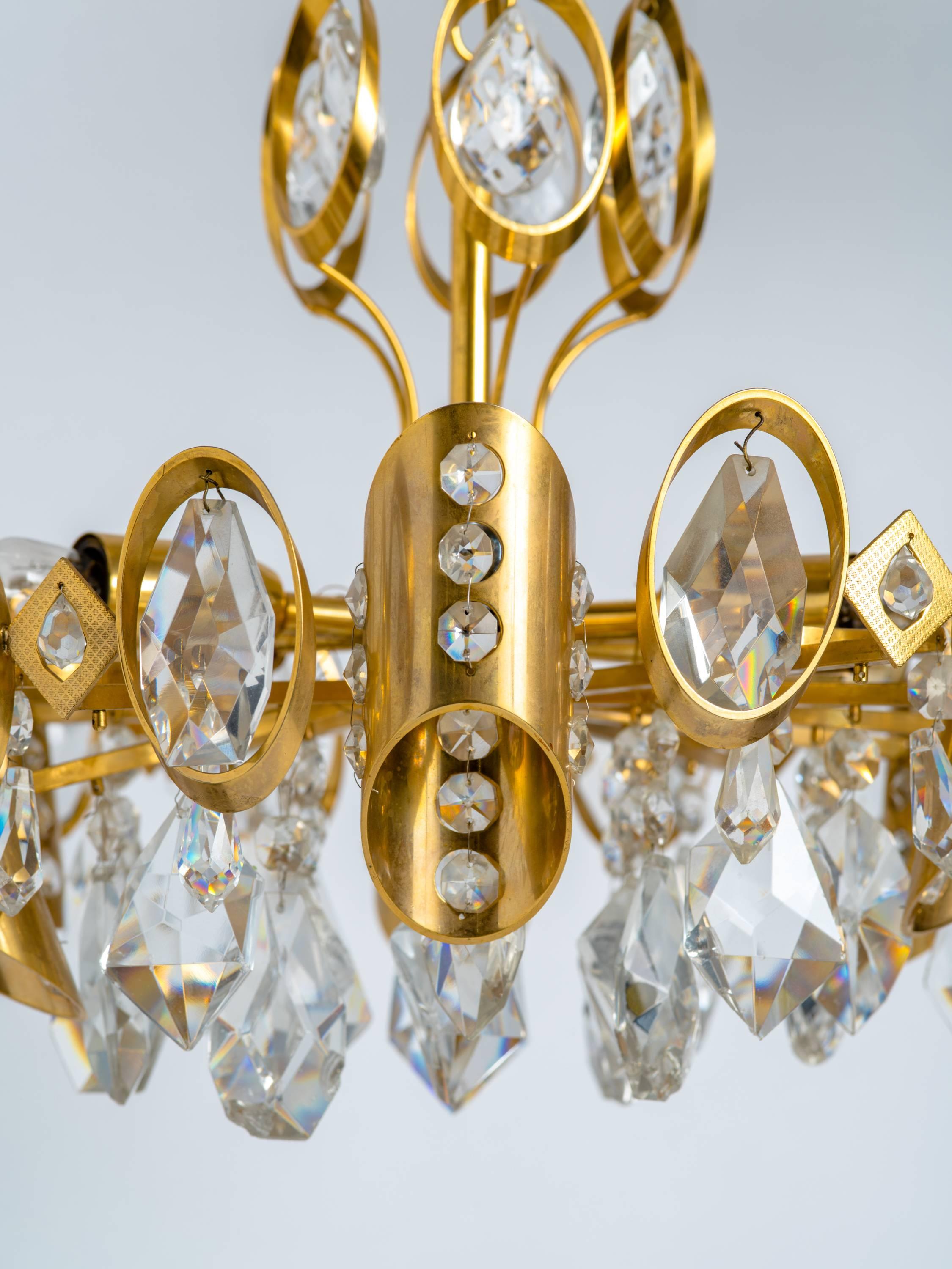 Atemberaubender Mid-Century Modern-Kronleuchter mit vergoldetem Messingrahmen und geschliffenen Kristallanhängern. Mehrstöckiges Design mit sechs radialen Lichtern und asymmetrischen Zylindern mit Perlenkristall-Akzenten.