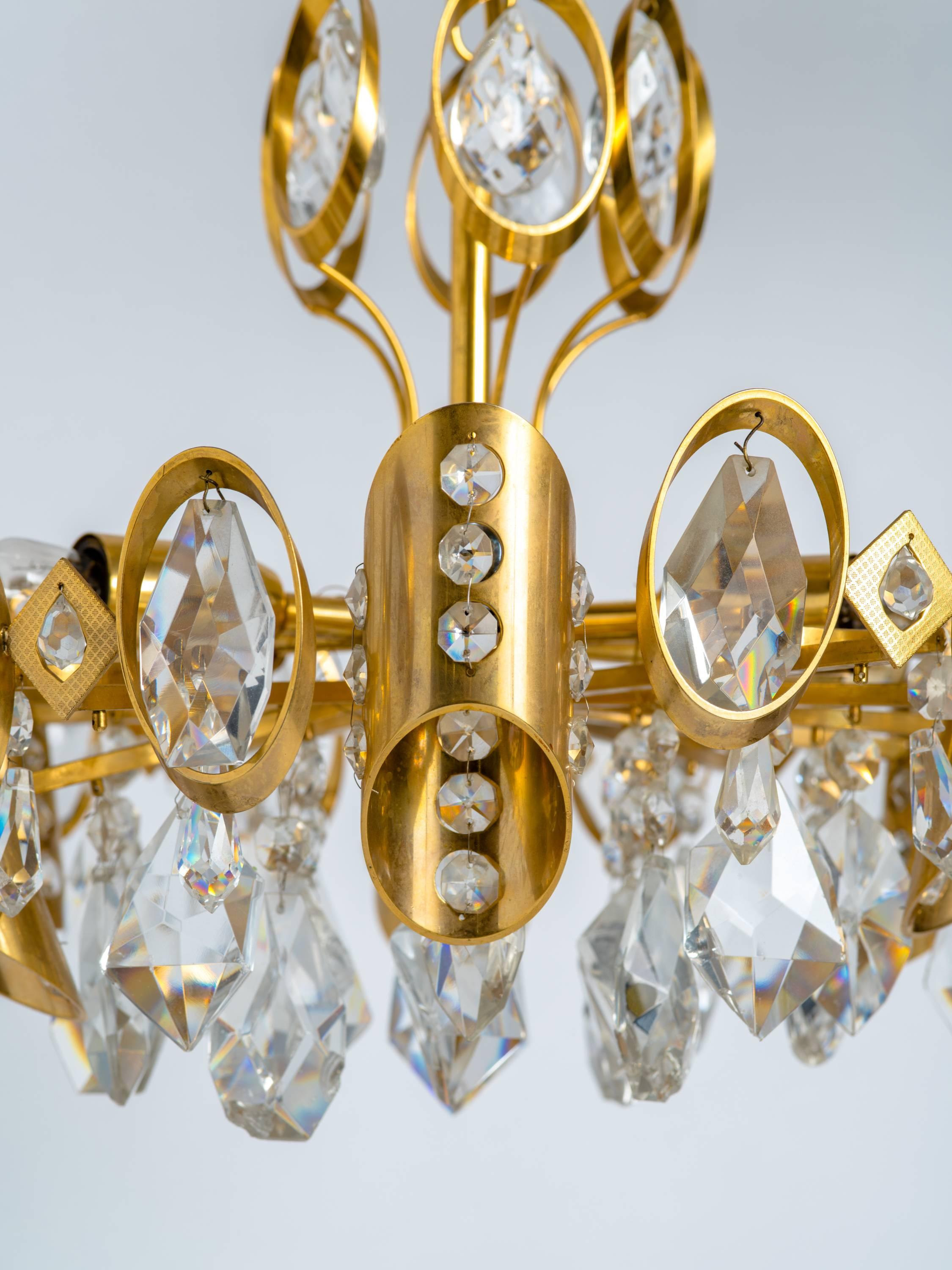 Piccolo lampadario Hollywood Regency in ottone dorato con pendenti in cristallo tagliato. Il design geometrico è caratterizzato da una serie di forme alternate: ovali, rombi e colonne inclinate, tutte dotate di prismi di cristallo o di perline di