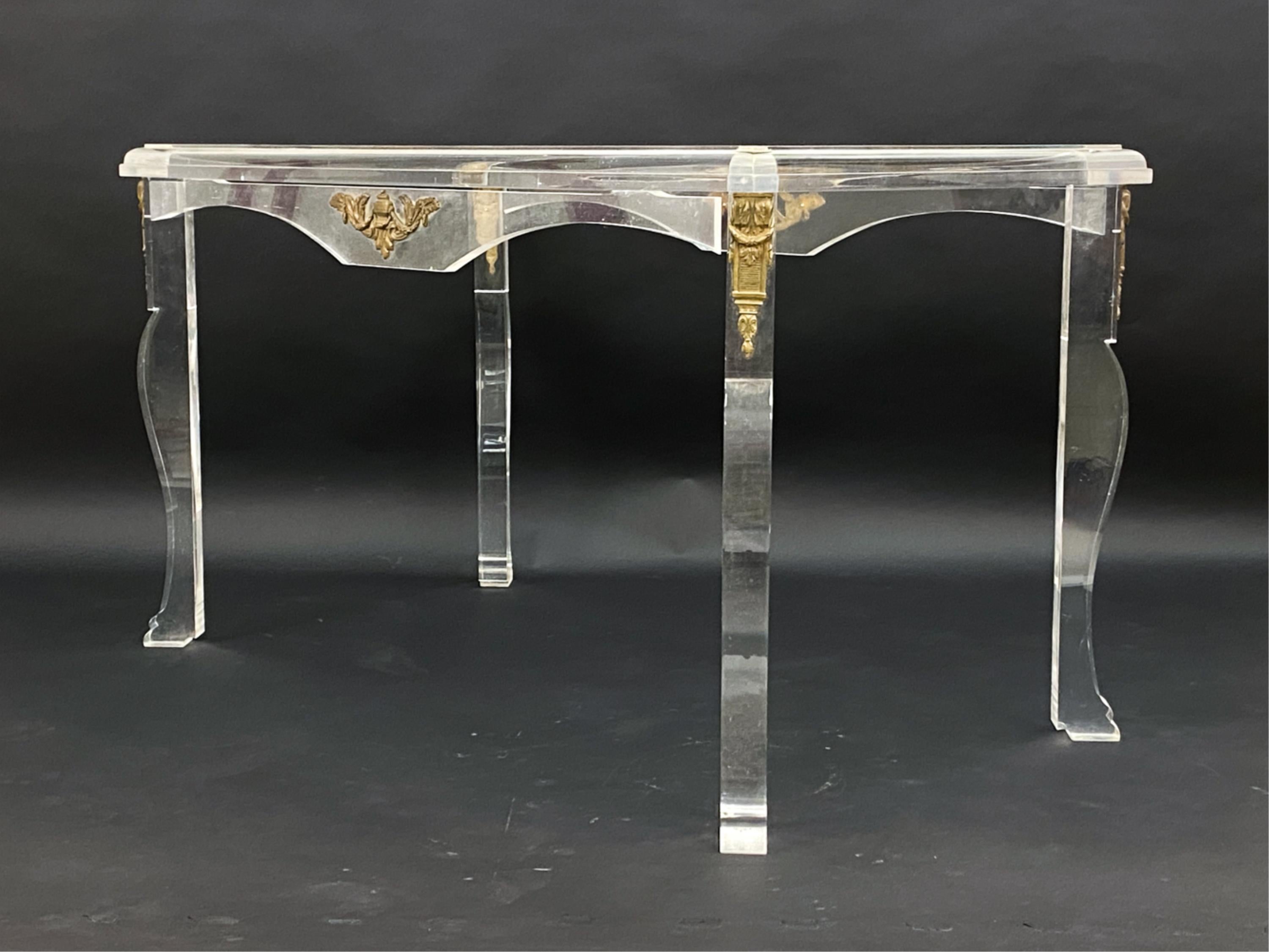 Questo elegante tavolino da caffè riporta all'epoca d'oro dello stile hollywoodiano dei primi anni del XX secolo. Realizzato in lucite di ottima fattura, questo tavolo con piano in vetro emana classe e stile: il suo aspetto sobrio gli permette di
