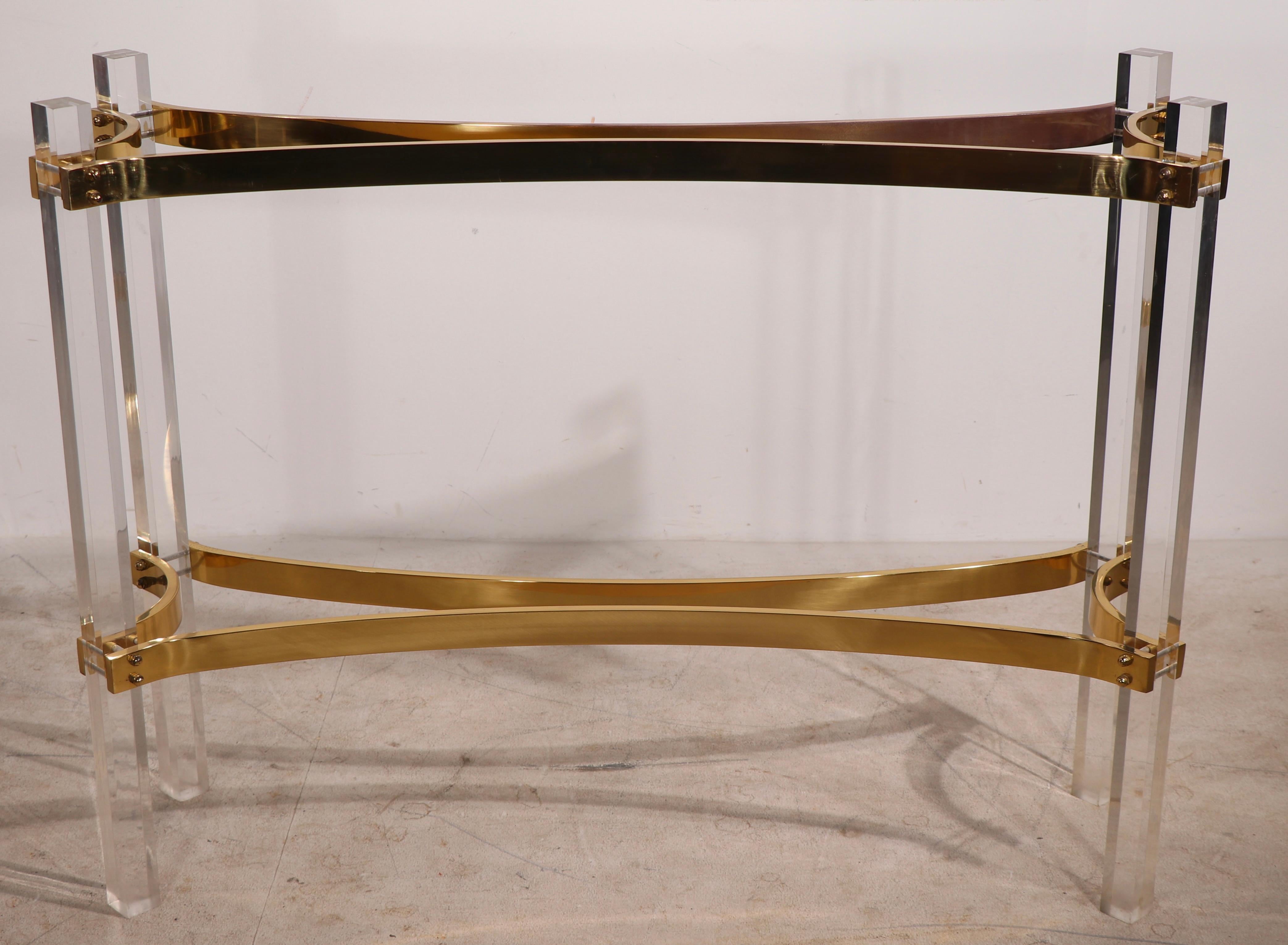 Exceptional lucite, brass and glass console table attributed to Charles Hollis Jones. The console features squared lucite legs, with arched brass stretchers that support two thick ( .75 in. ) plate glass shelves. This piece is of extraordinary