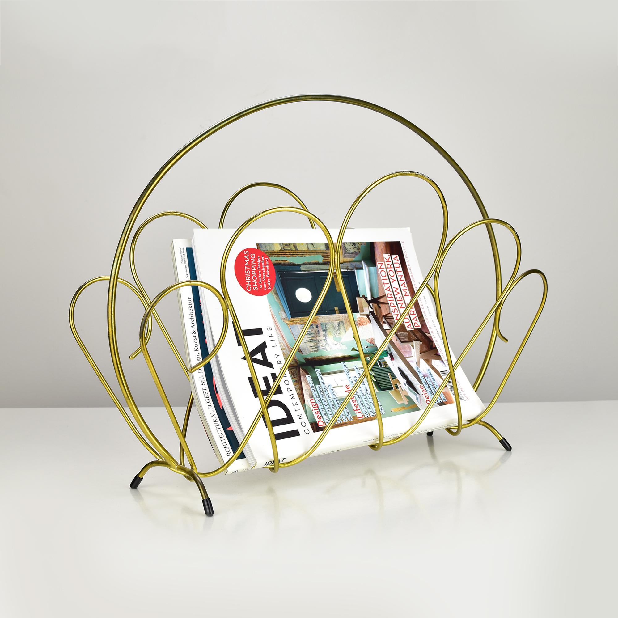Questo elegante portariviste Hollywood Regency degli anni '60 incarna l'estetica glamour di metà secolo con il suo design scultoreo in filo d'ottone. Caratterizzato da anelli e curve intrecciate, lo stand presenta una struttura ariosa e decorativa