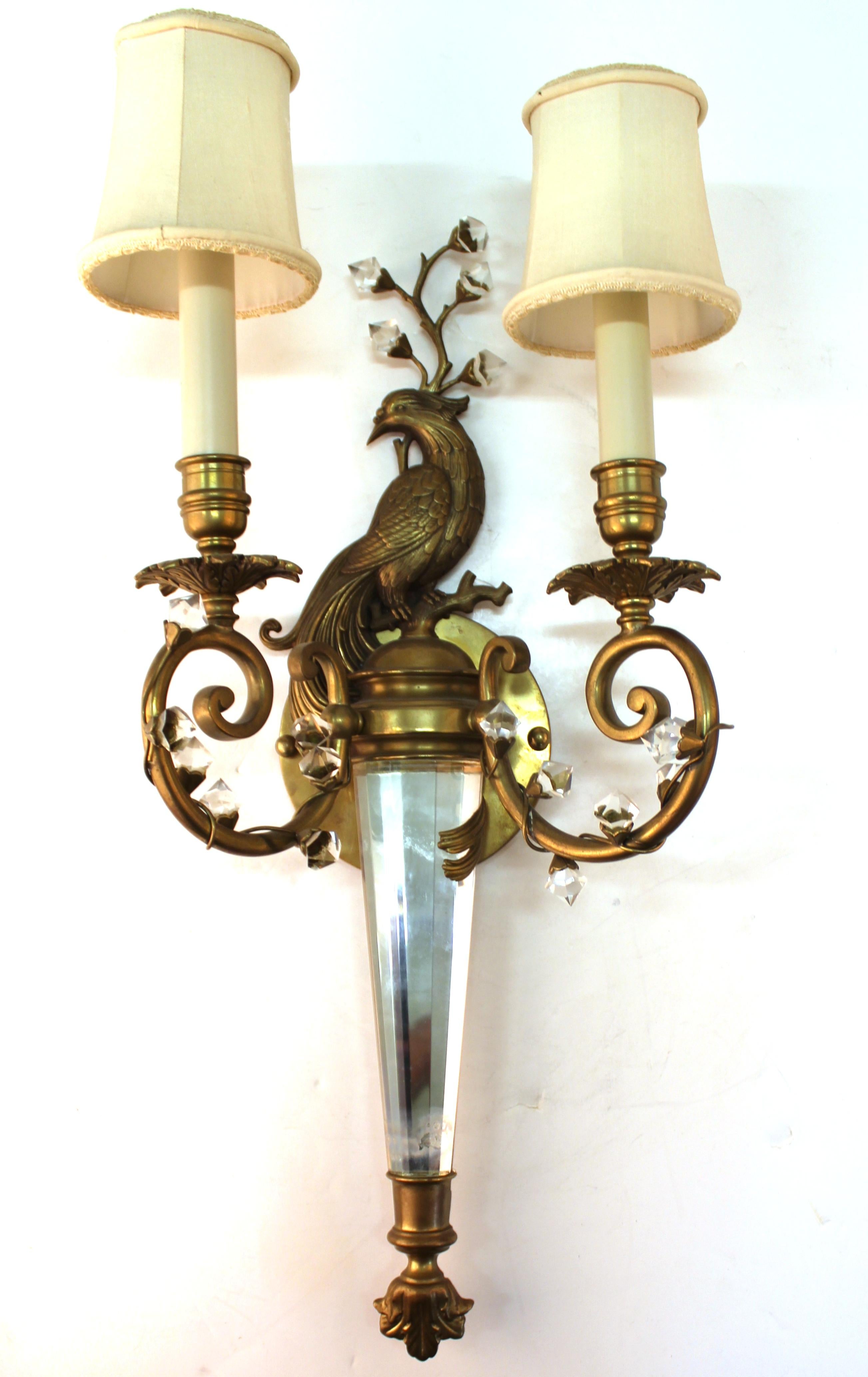 Hollywood Regency brass and crystal wall sconce in the style of Maison Baguès, with a bird sitting amidst crystal foliage wrapped around two arms holding up lights. One large piece of crystal used as a decorative stem. The piece is in great vintage