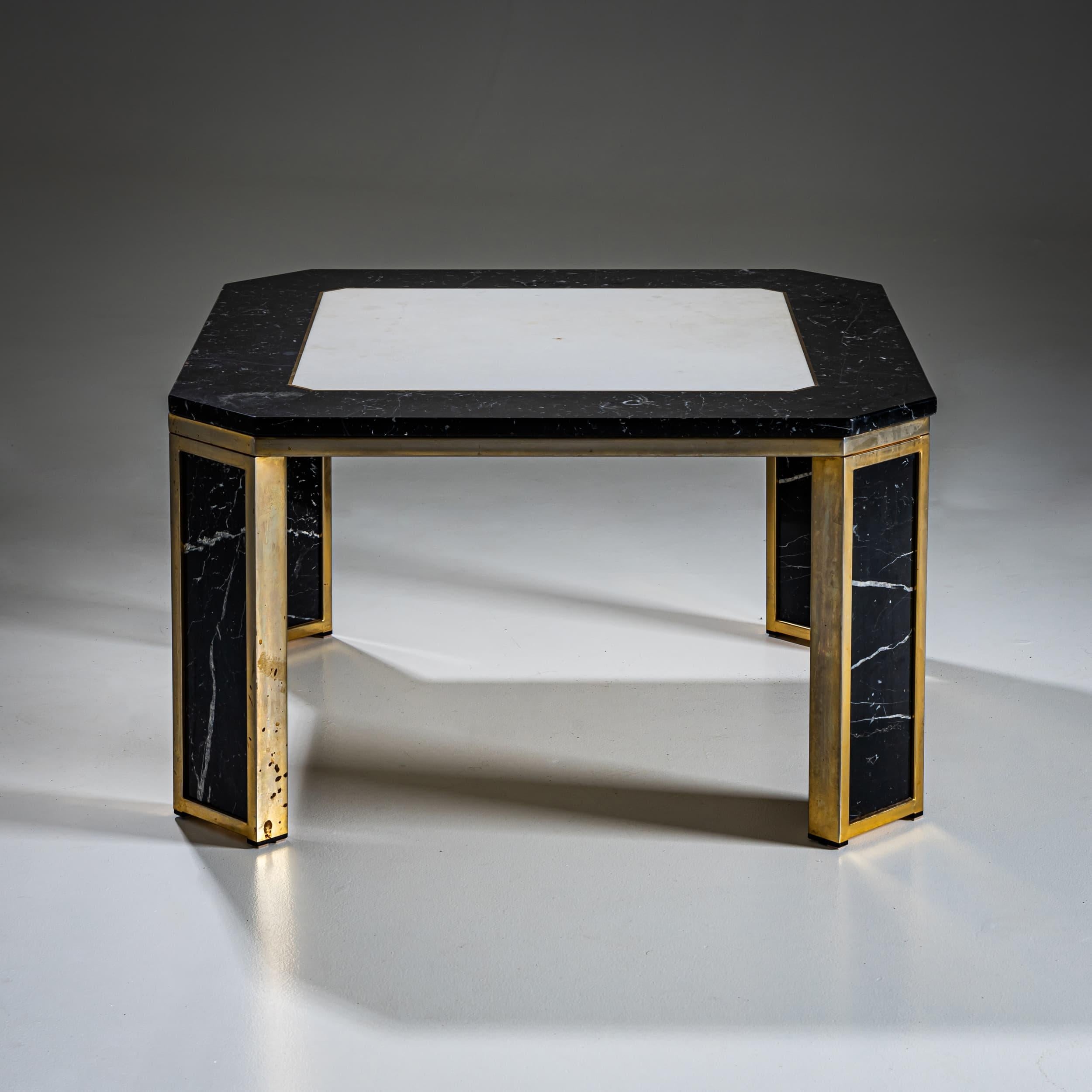 Table basse octogonale avec un plateau en marbre noir veiné de blanc et une incrustation centrale de pierre claire. La base en laiton épurée offre un contraste saisissant avec le marbre aux motifs riches, conférant à la table une présence audacieuse