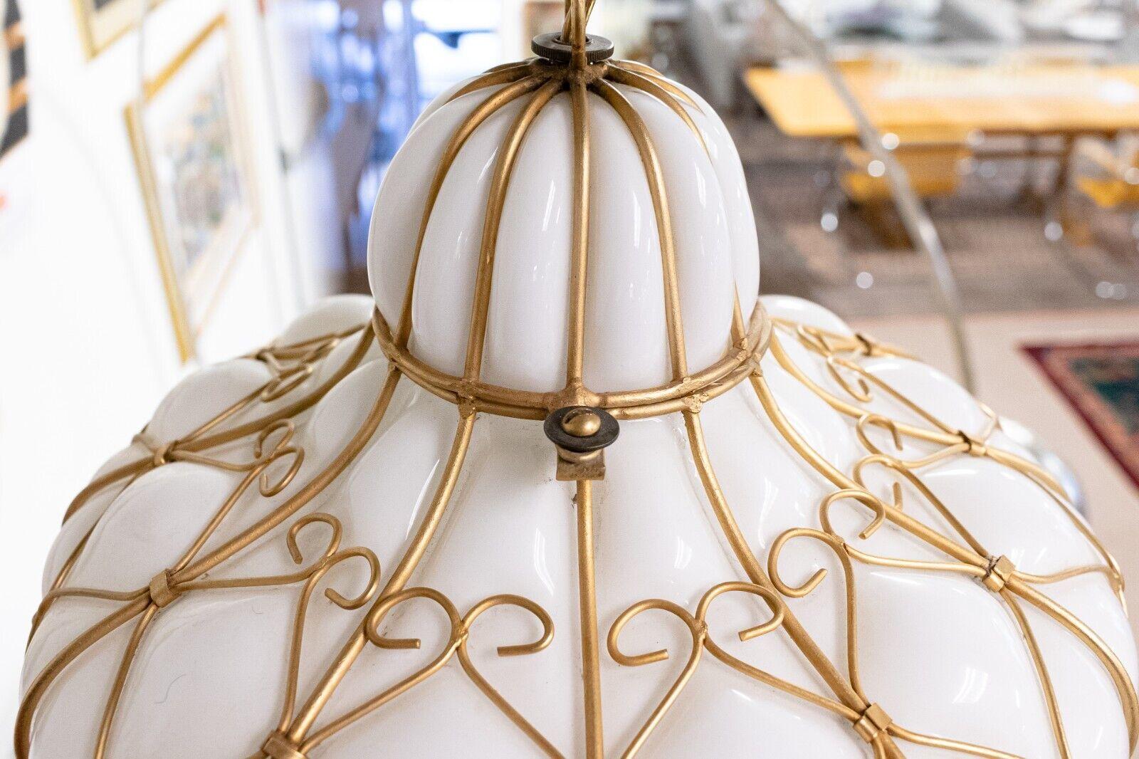 A hollywood regency milk glass caged teardrop light fixture. This is a wonderful pendant light fixture that features a gorgeous white milk glass construction, and a gilded sculptural frame around that. This piece hangs from an extra long matching