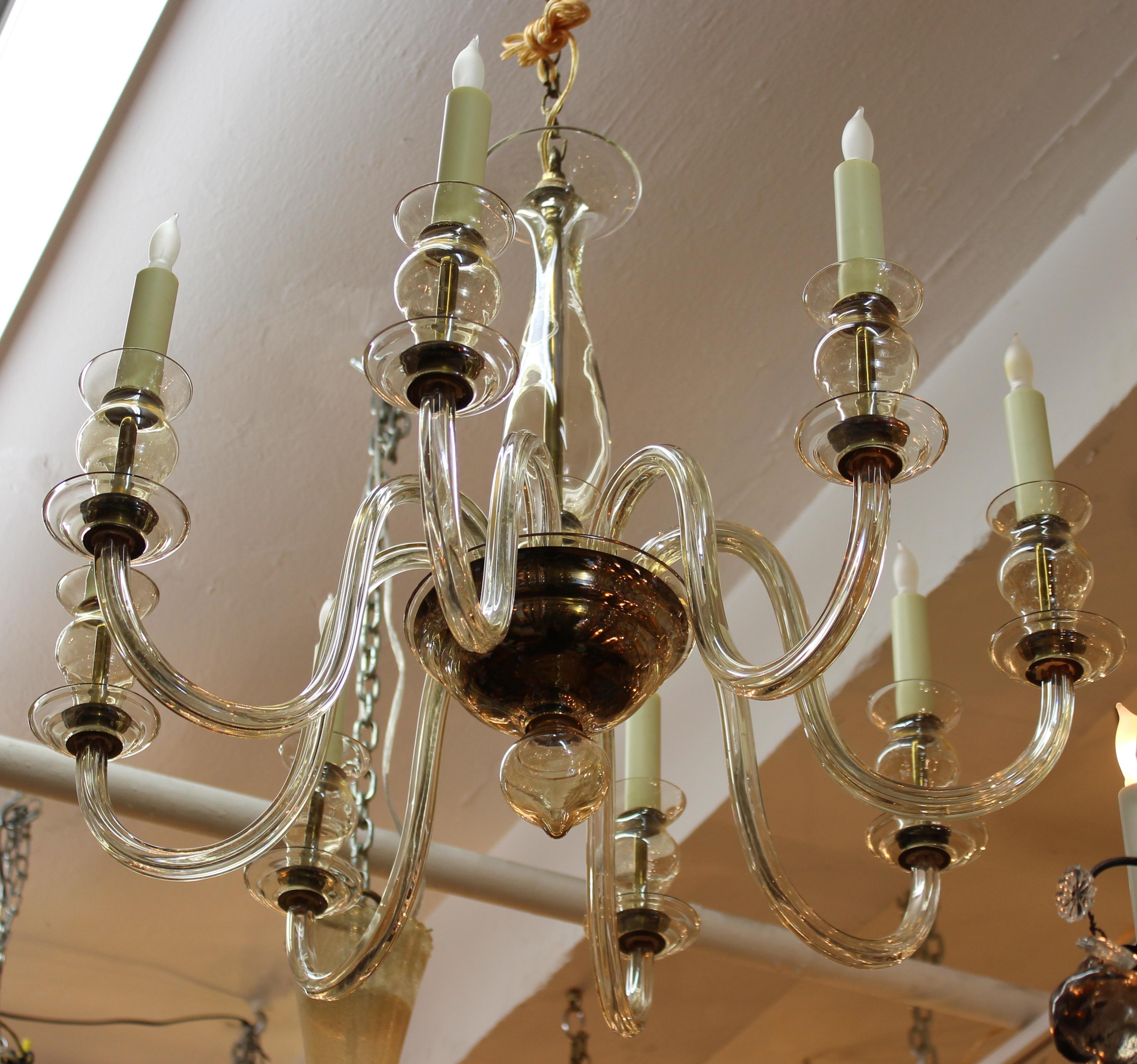 Hollywood Regency chandelier in light amber Murano glass. The chandelier features eight curved arms with faux candle sockets, a vase shaped body and an onion dome finial at the bottom. Despite some small chips to the canopy of the body the