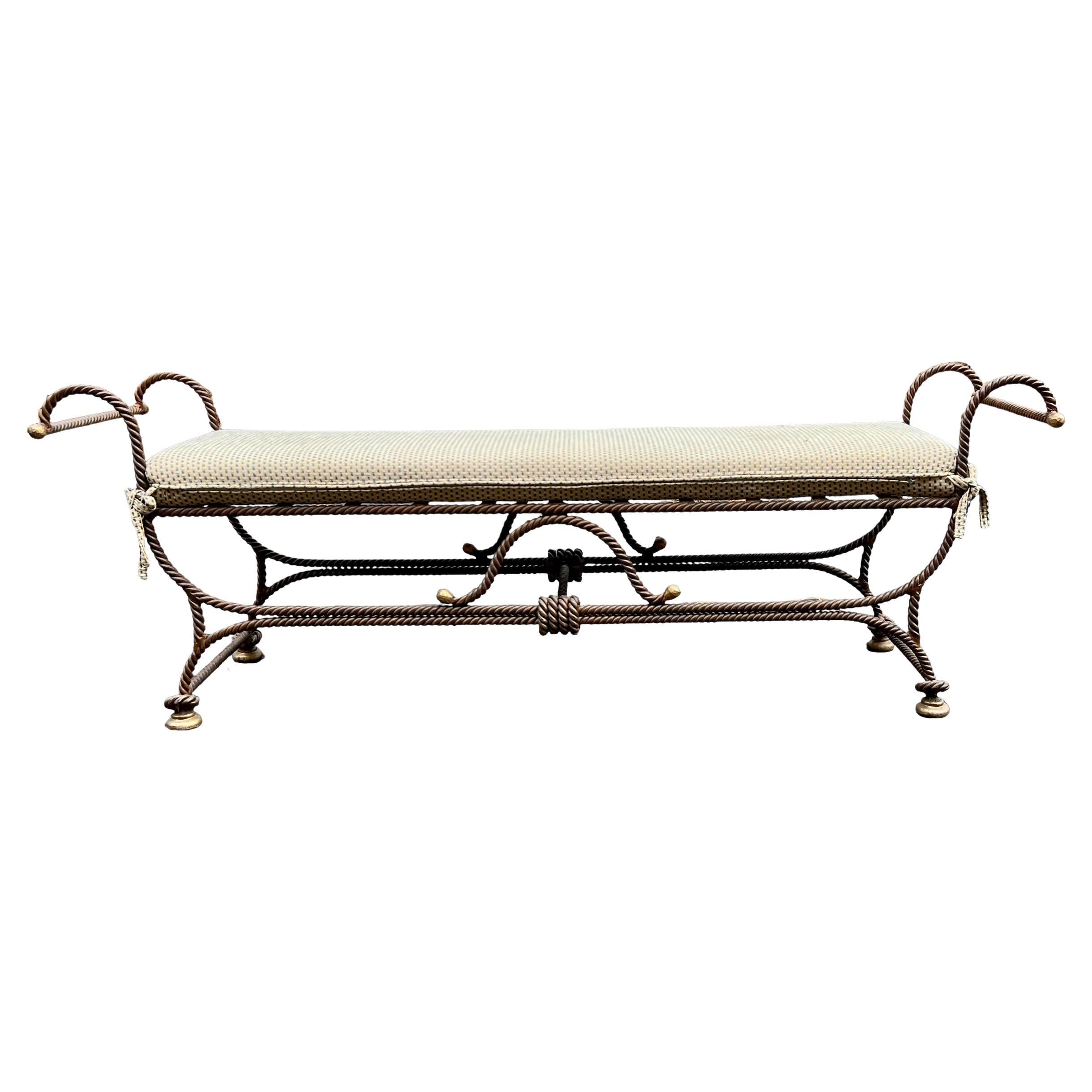 This is a Hollywood Regency Era wrought Iron Neo-Classical style bench with rope and tassel motif. The piece is very heavy, and the Swiss dot cotton fabric cushion is vintage. The iron does have gilt accents. It is in very good condition and most
