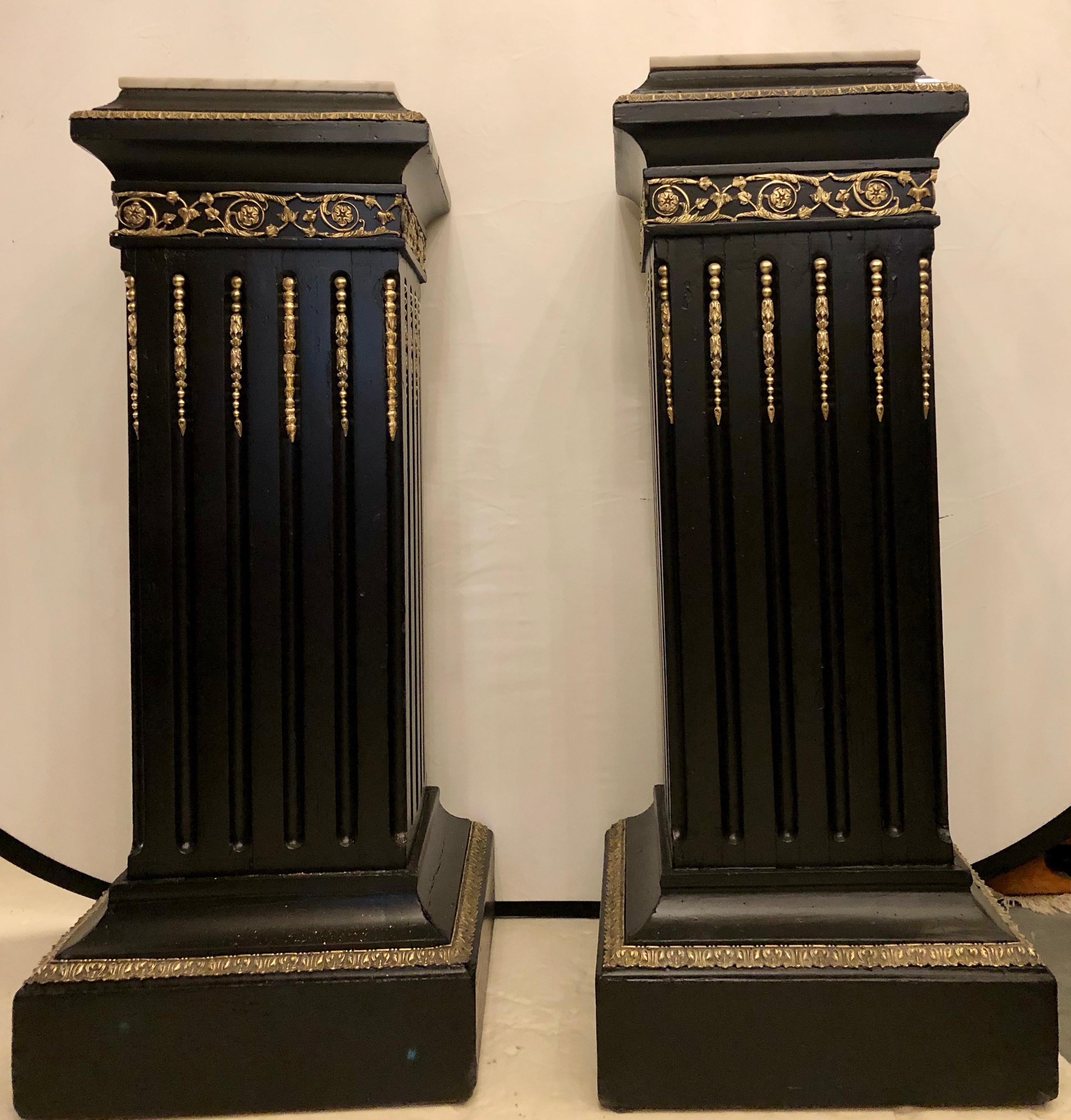 Pair of Hollywood Regency neoclassical ebony pedestals. Each having bronze mounts and white marble tops. This strong sturdy pair of column form stylized pedestals are certain to enhance any piece of art work or culture which sits upon them.
 