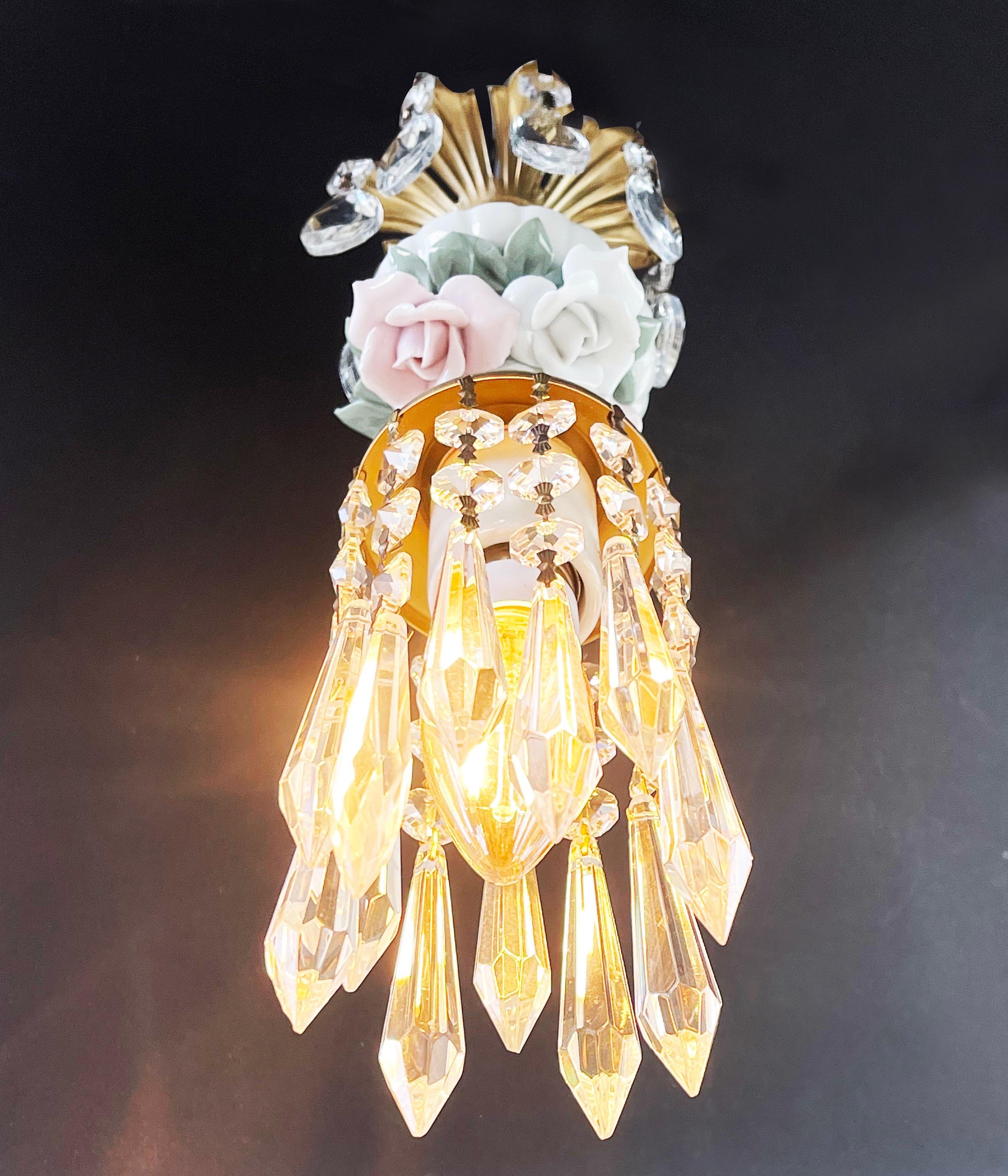 Wunderschöner, lebendiger 1-Licht-Kronleuchter mit geschliffenen Glastropfen in Kristalloptik.
Hergestellt aus Toleware mit einer matten, messingfarbenen Oberfläche, mit pastellrosa und weißen, handgefertigten Rosenblüten aus Porzellan, 
auf