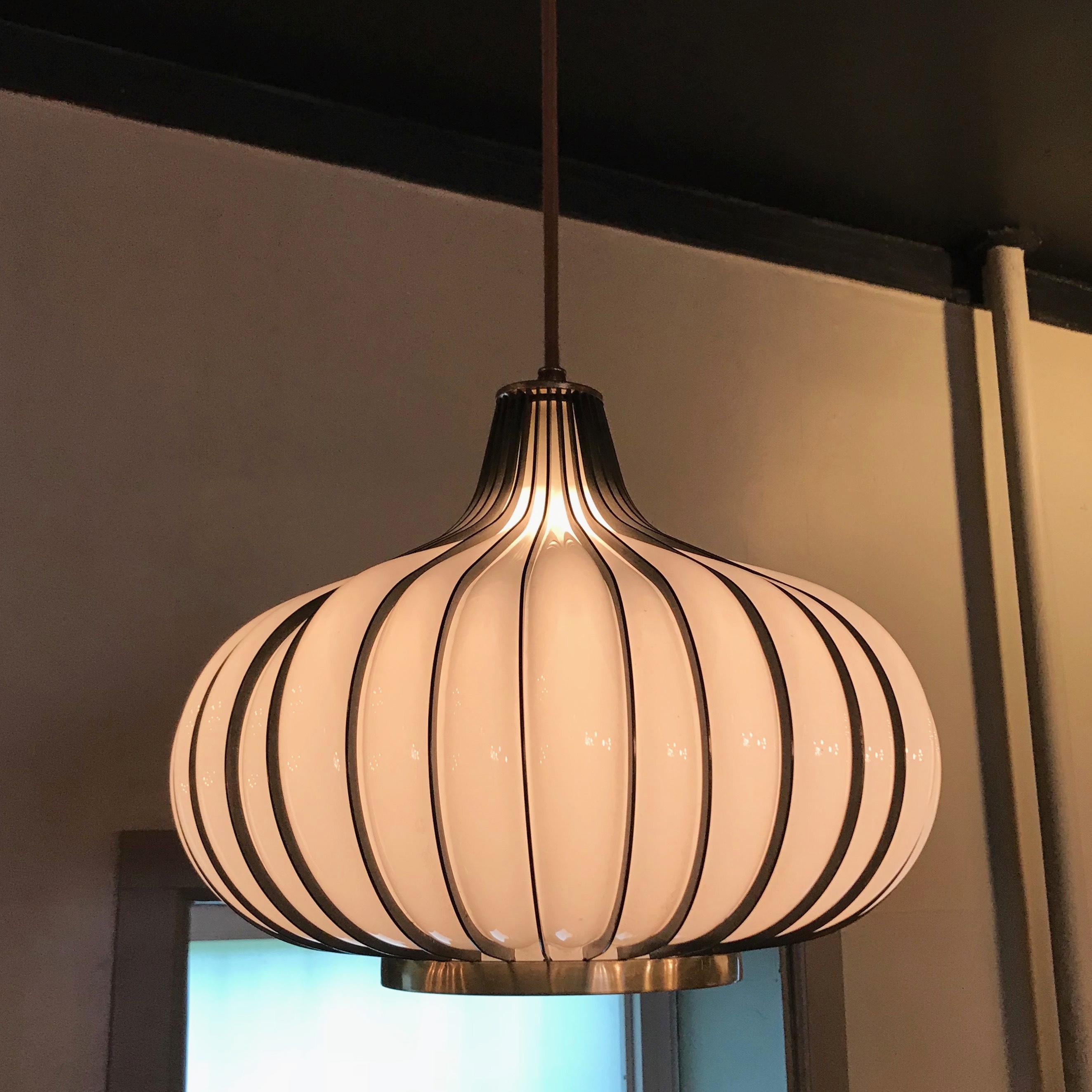 Midcentury, Hollywood Regency, garlic or onion shaped, swag, pendant light features a blown milk glass shade encased in a brass-toned, steel frame. The pendant is newly wired with 6 feet of thick brown cloth cord.