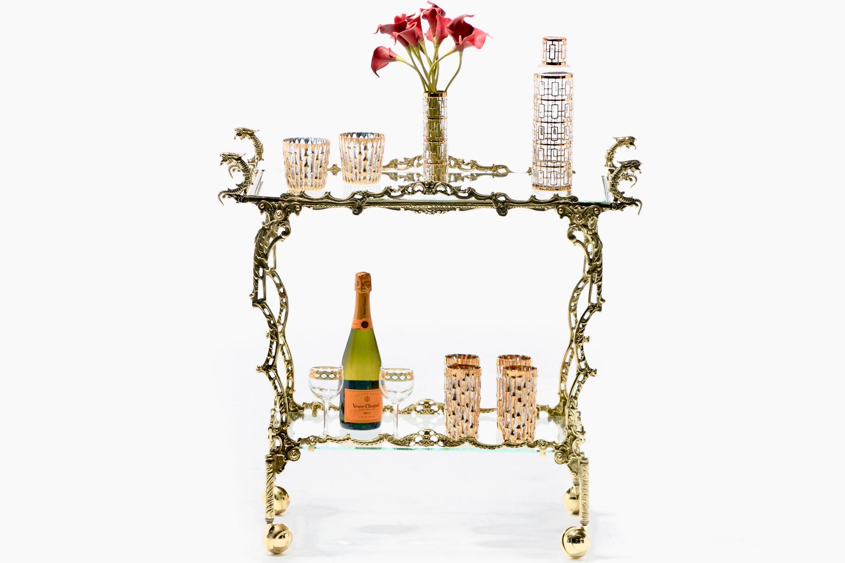 This chic bar cart is most certainly not the shy one in the room with an ornate dragon themed frame of golden brass that's attention grabbing without apology. Cast brass dragon heads dominate the silhouette like old money gargoyles. Frame is