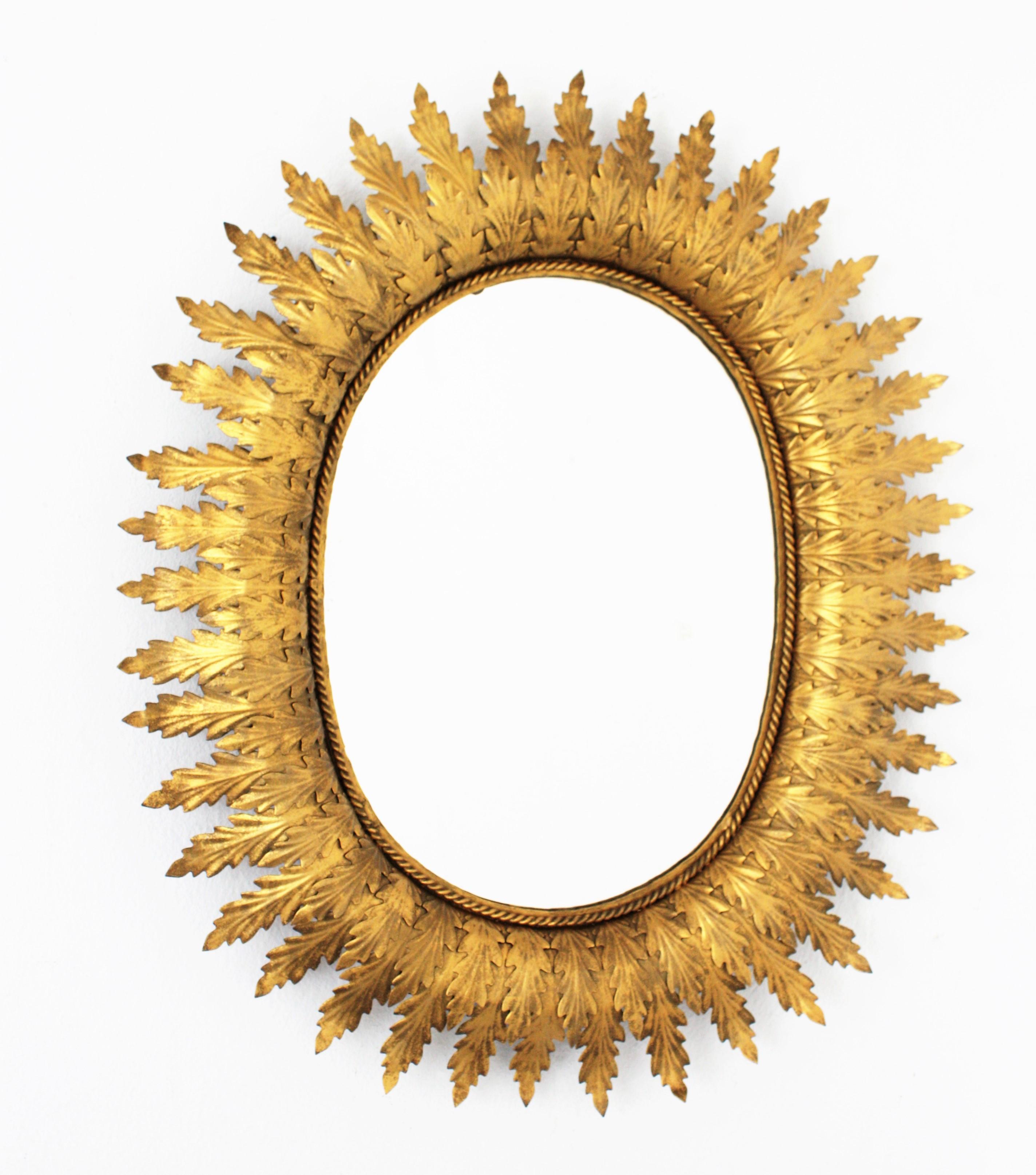 Lovely gilt metal oval shaped sunburst mirror in the Hollywood Regency style. The frame is comprised of a series of overlaying leaves in two sizes and joined together with a twisted braiding. Spain, 1950s.
Glass dimensions: 39cm H; 30cm W.
 