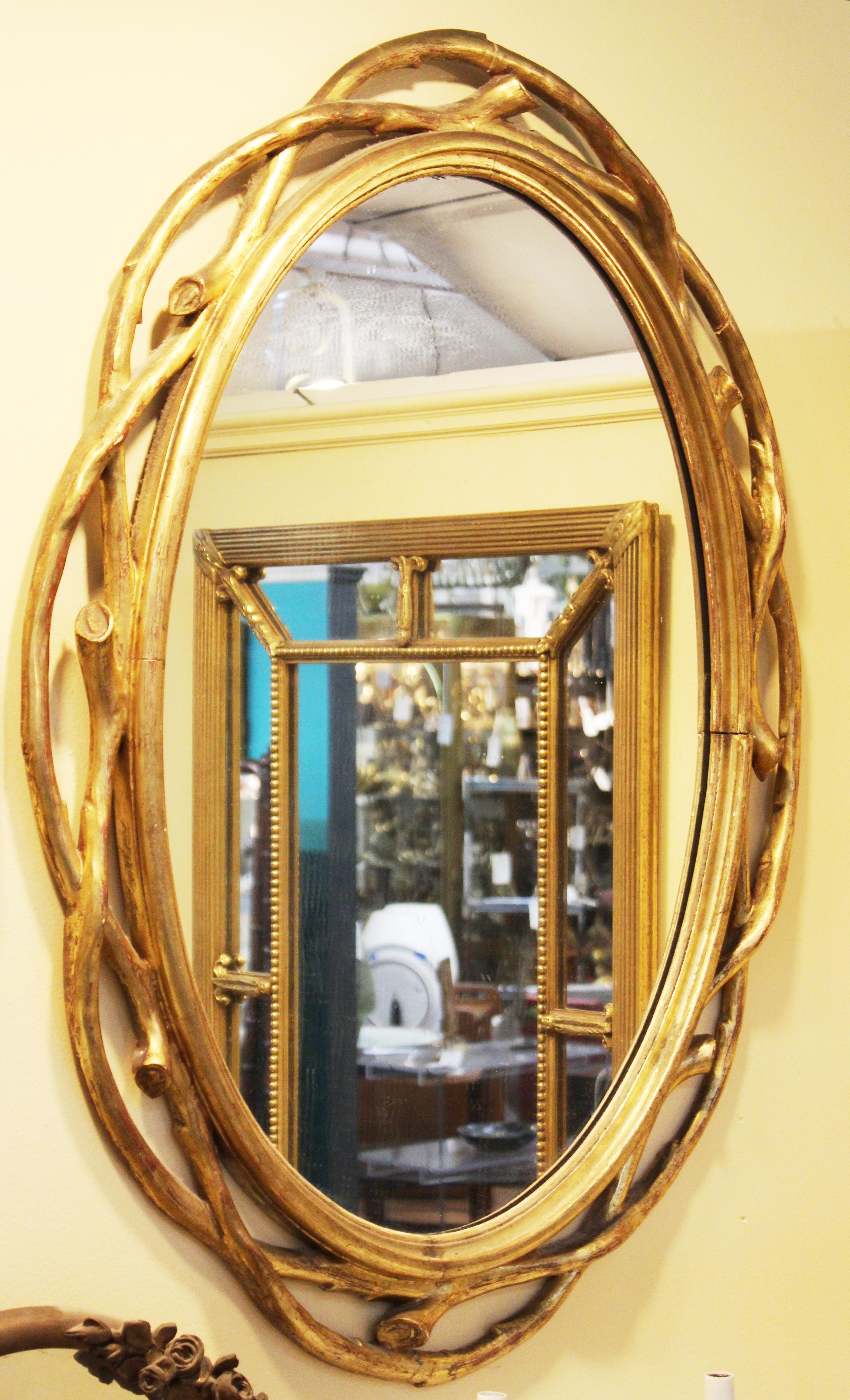 Hollywood Regency pair of large oval mirrors with carved giltwood frames in the shape of wreaths of wooden branches. The pair is in great vintage condition with age-appropriate wear and use and some age-related minor cracks to the frames.