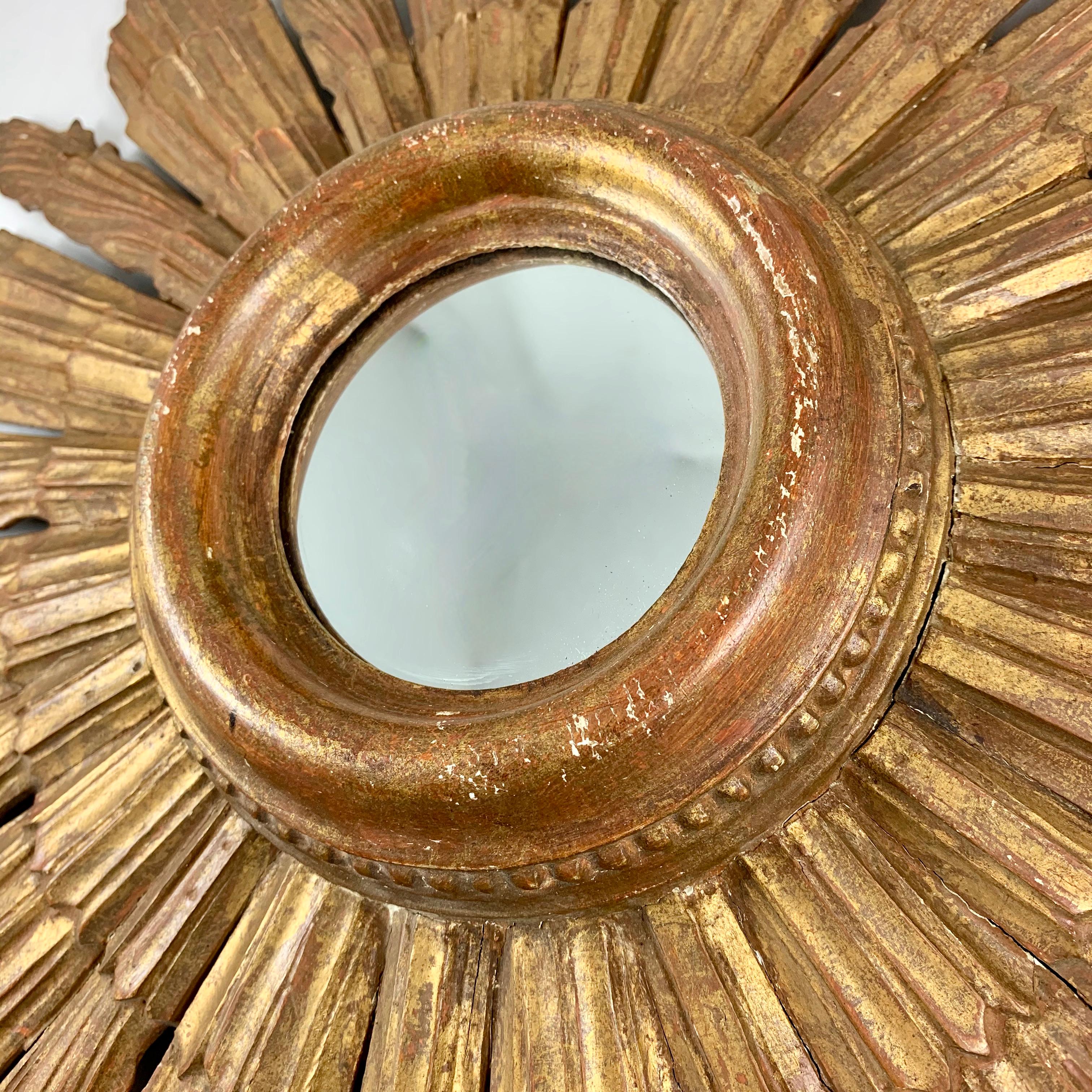 A large Hollywood Regency period wall mirror, showing a giltwood sunburst with a raised and beaded bezel, from France, circa 1920s.

Made of gilded and gesso on wood, the mirror is set in a wide, raised and beaded bezel painted in gold with red