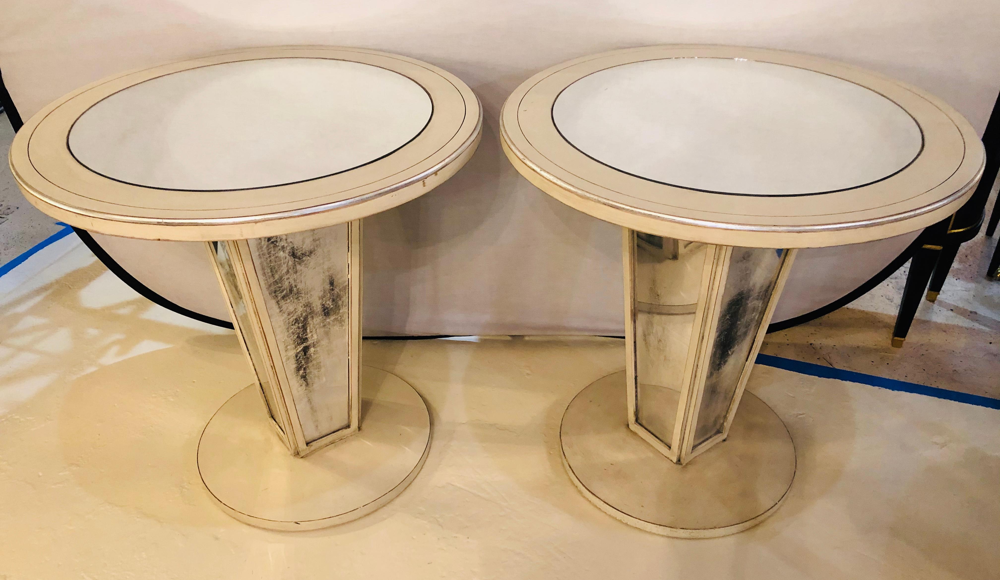 Hollywood Regency paint decorated mirrored side, end or lamp tables. A pair of exquisite tables having a clean mirror top in a painted circular frame supported by a square tapering base of distressed mirror form flanked by a wooden painted frame on