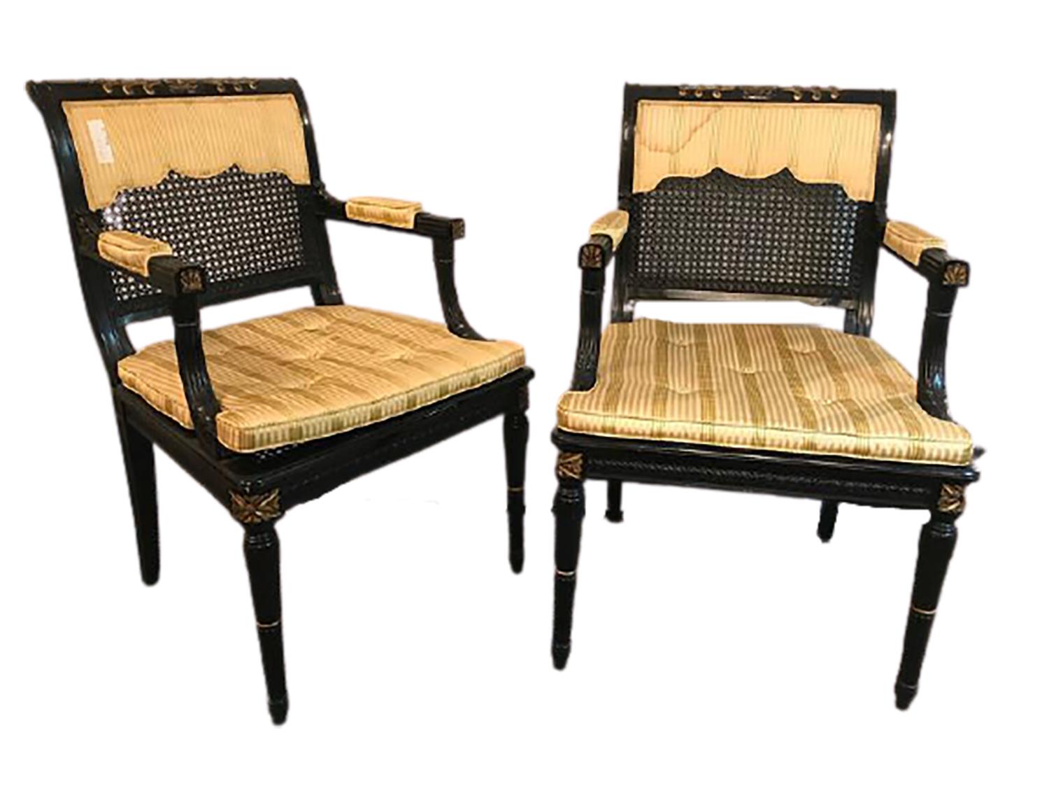 Pair of black and gold cane back armchairs, Fauteuils attributed Maison Jansen. Each ebonized frame with fine gold decorative high lights. The pair having cushion seats with drapery half covered back rests (one with a slight stain pictured) with