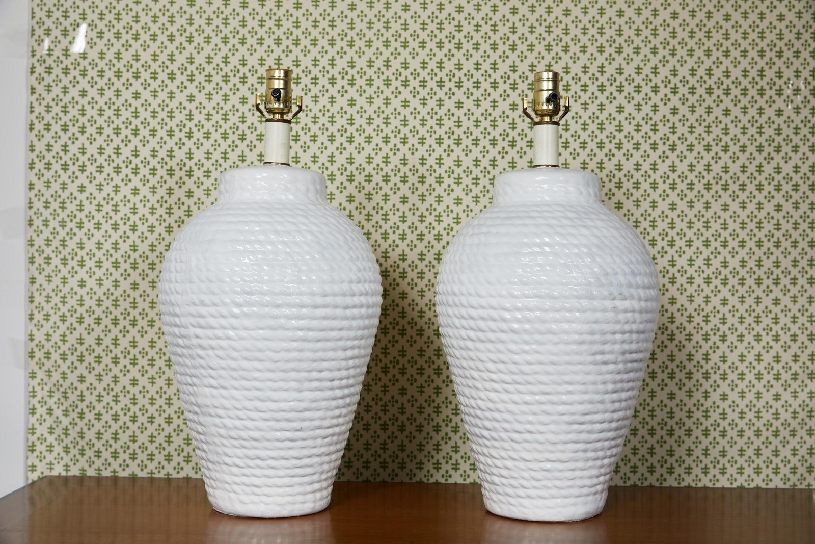 Mid-20th century pair of white ceramic table lamps shaped like urns and having a cast rope motif. They are created in the style of Hollywood Regency.