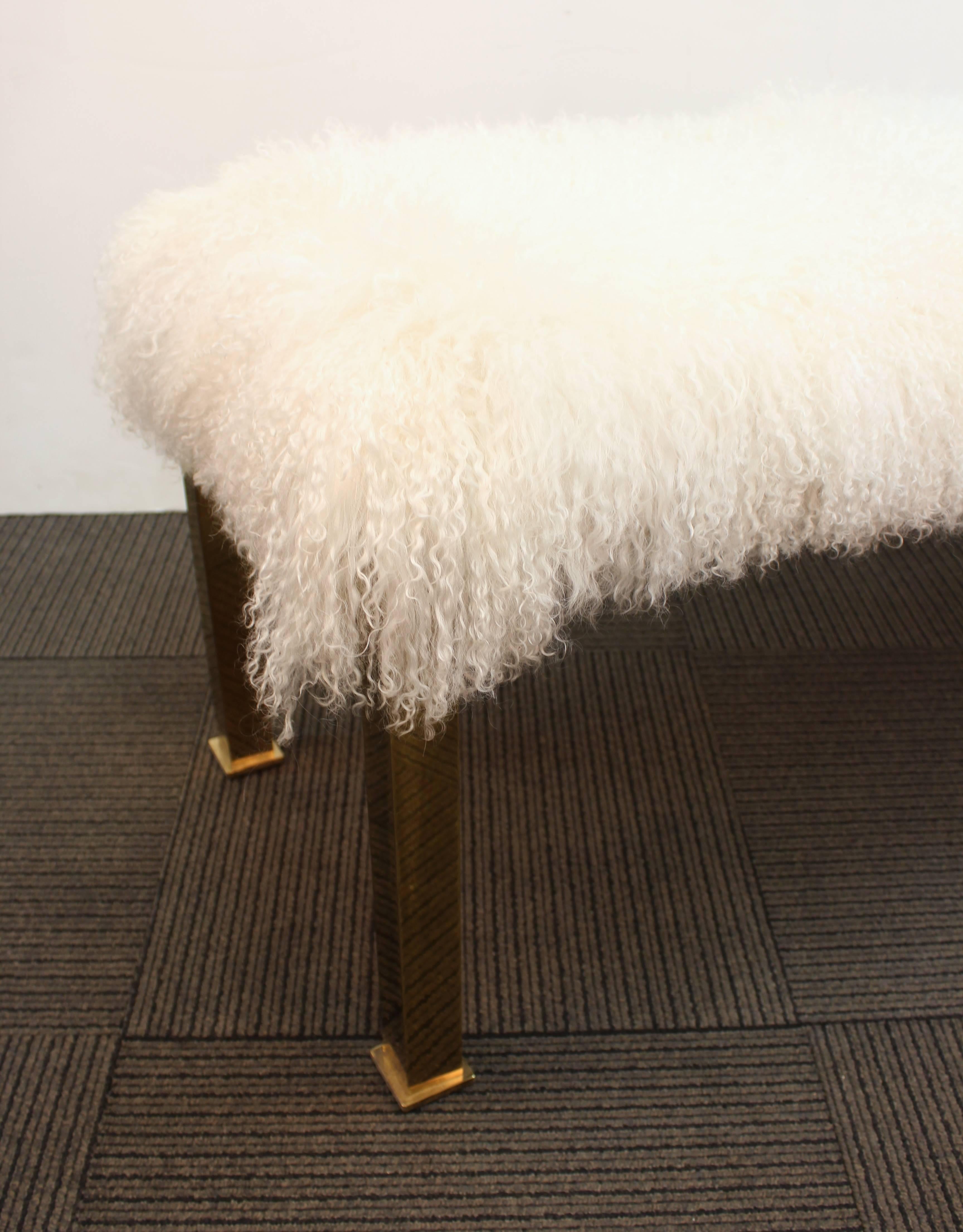 Hollywood Regency Parsons style bench with polished brass legs and curly Mongolian lambs wool upholstery. The legs feature a stepped detail. This piece is in good vintage condition and has wear consistent with age and use.