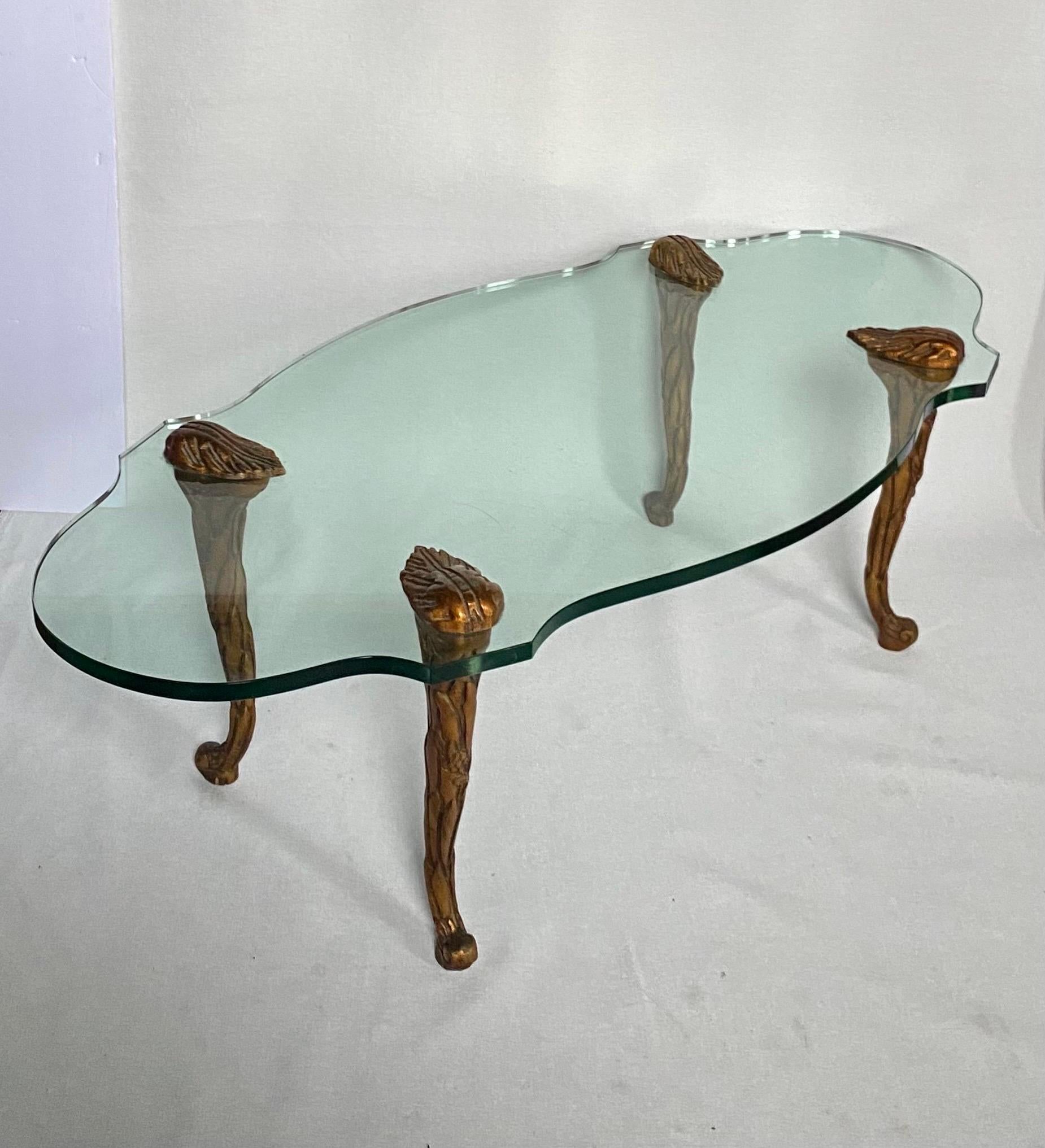 Elegant Mid Century oval form coffee table in the style of P.E. Guerin.  This Hollywood Regency style cocktail table features a thick glass top held aloft by four carved giltwood palm foliate motif cabriole legs. 