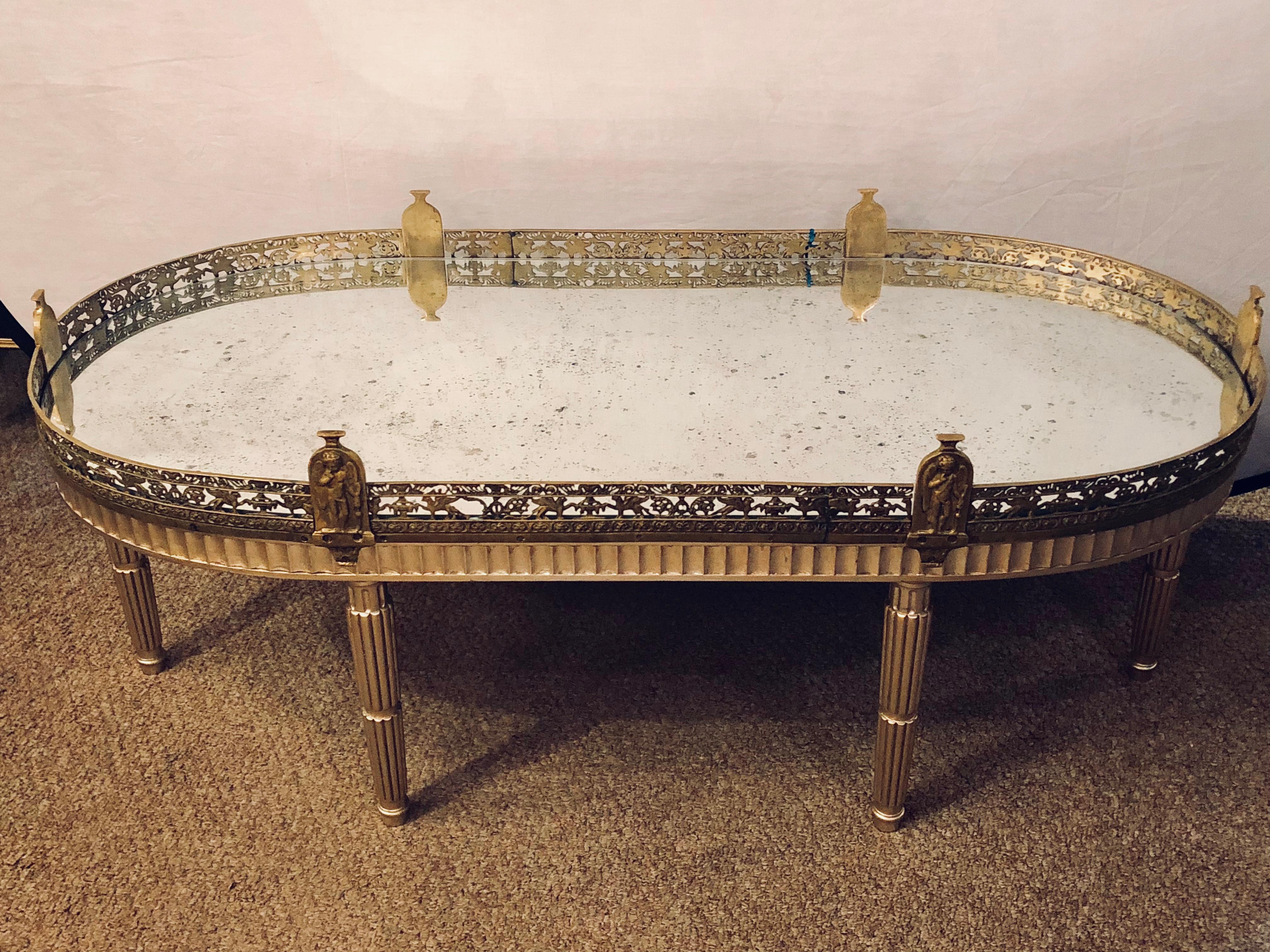 Hollywood Regency plateau style coffee table in Louis XVI manner finished in a silver gilt. Stunning silver form on a Louis XVI style base having a reeded apron with an antiqued mirror top set inside a bronze galleried frame. The bronze frame