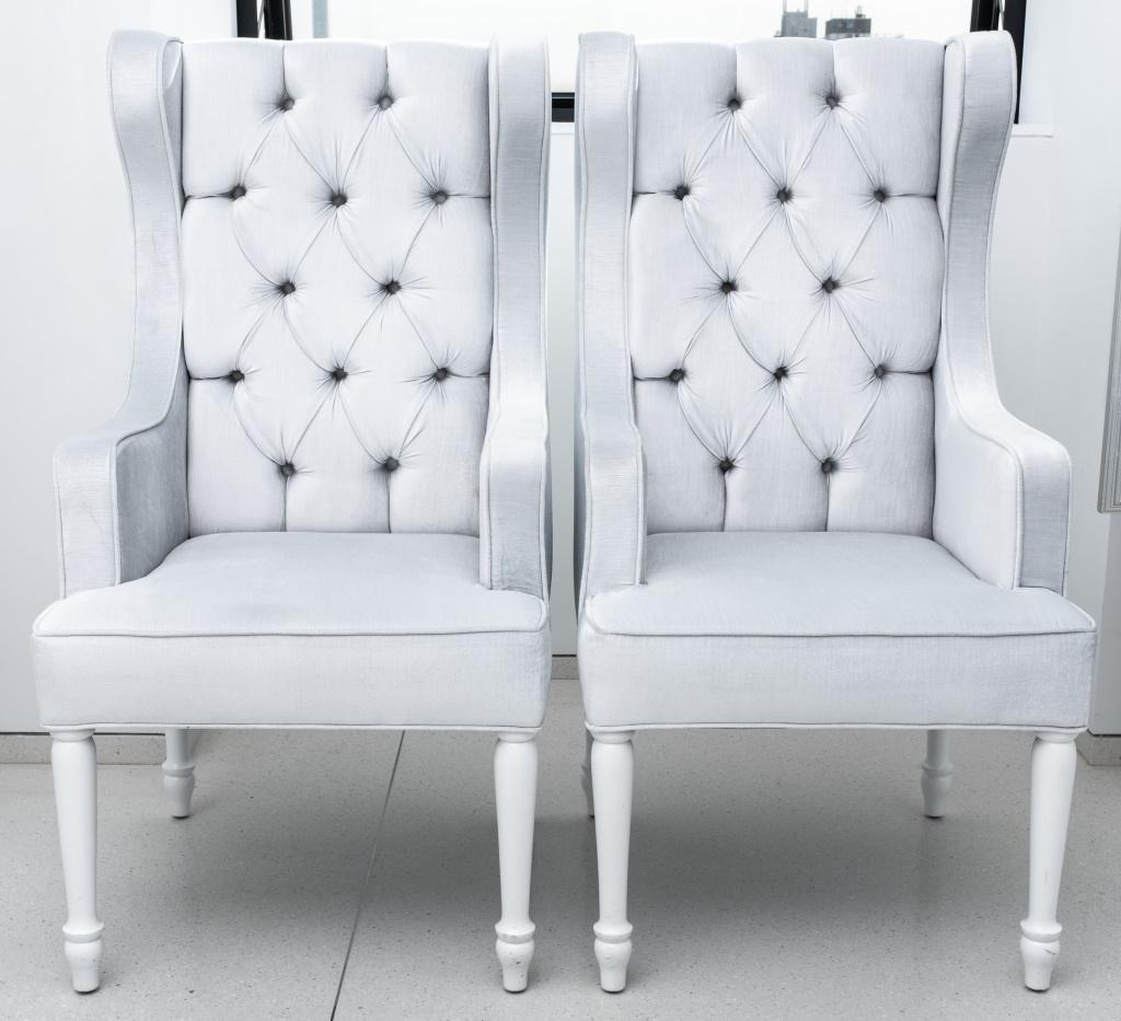 Pair of Hollywood Regency platinum buttoned velvet upholstered wing chairs, with square backs and seats, each on four turned white-painted legs. 46