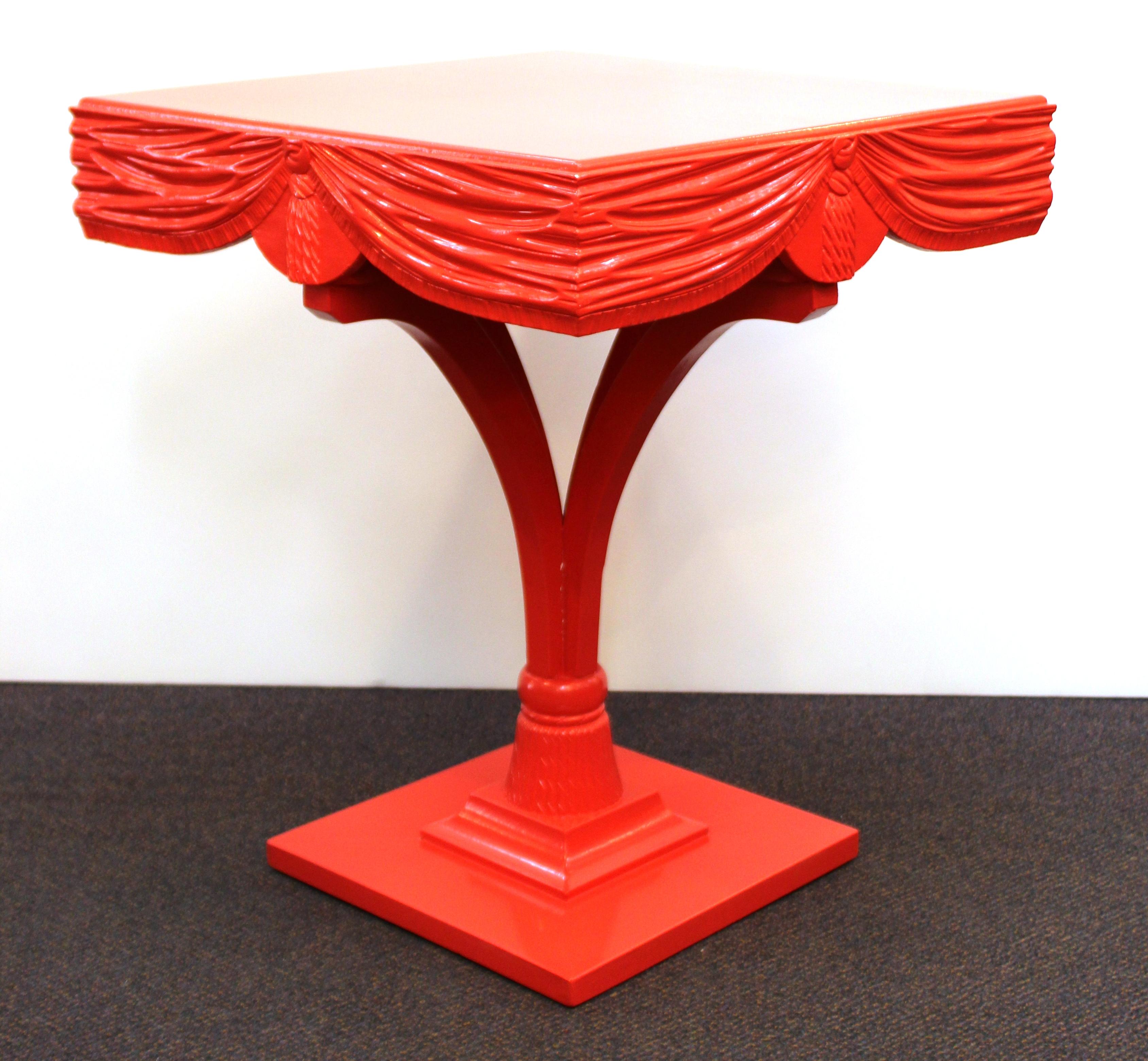 Hollywood Regency pair of red painted wood side tables with ornately carved drapery. The pair has recently been repainted and is in great vintage condition with very minimal wear to the surfaces.